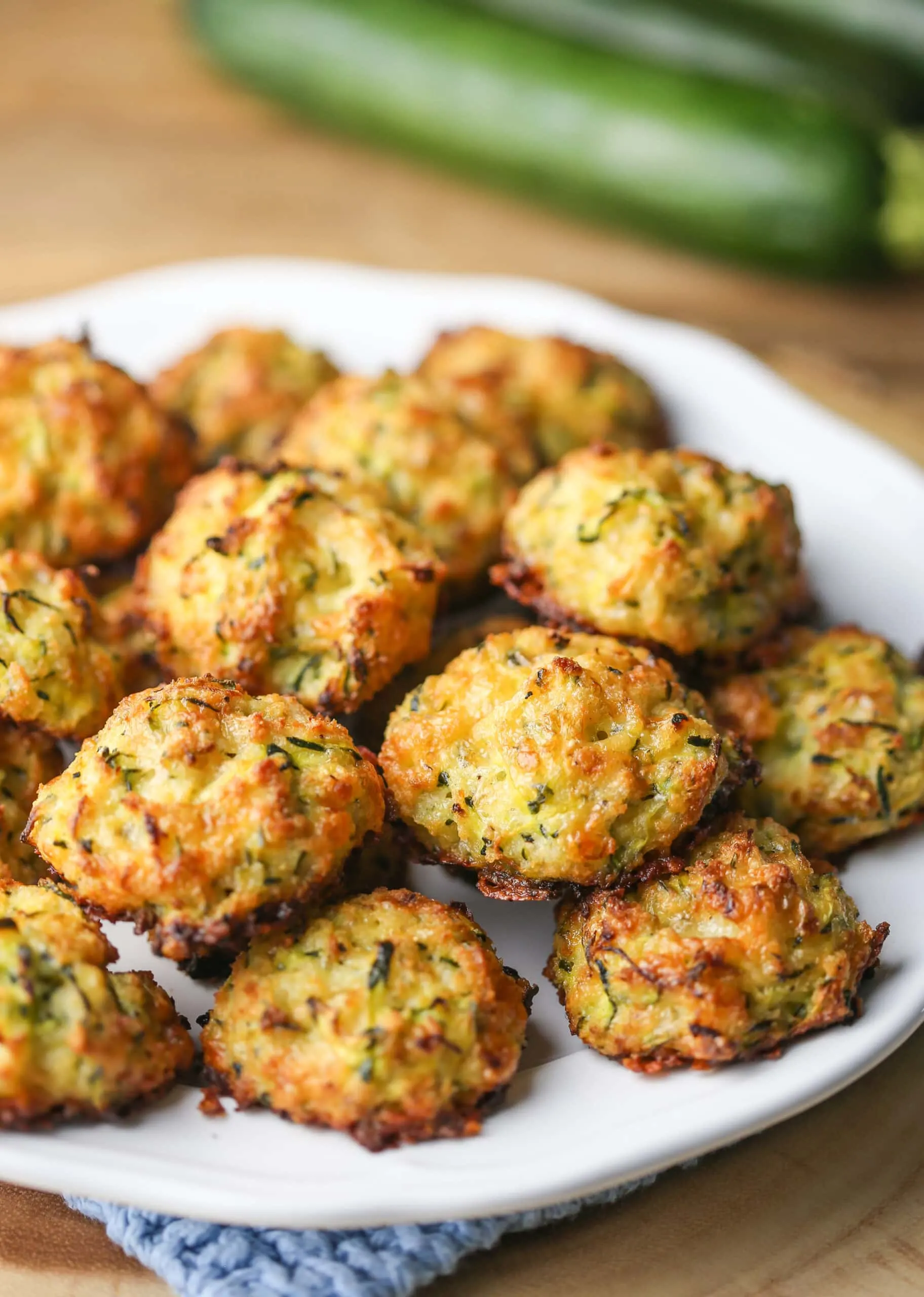 Golden-brown cheesy baked zucchini bites on a white plate.