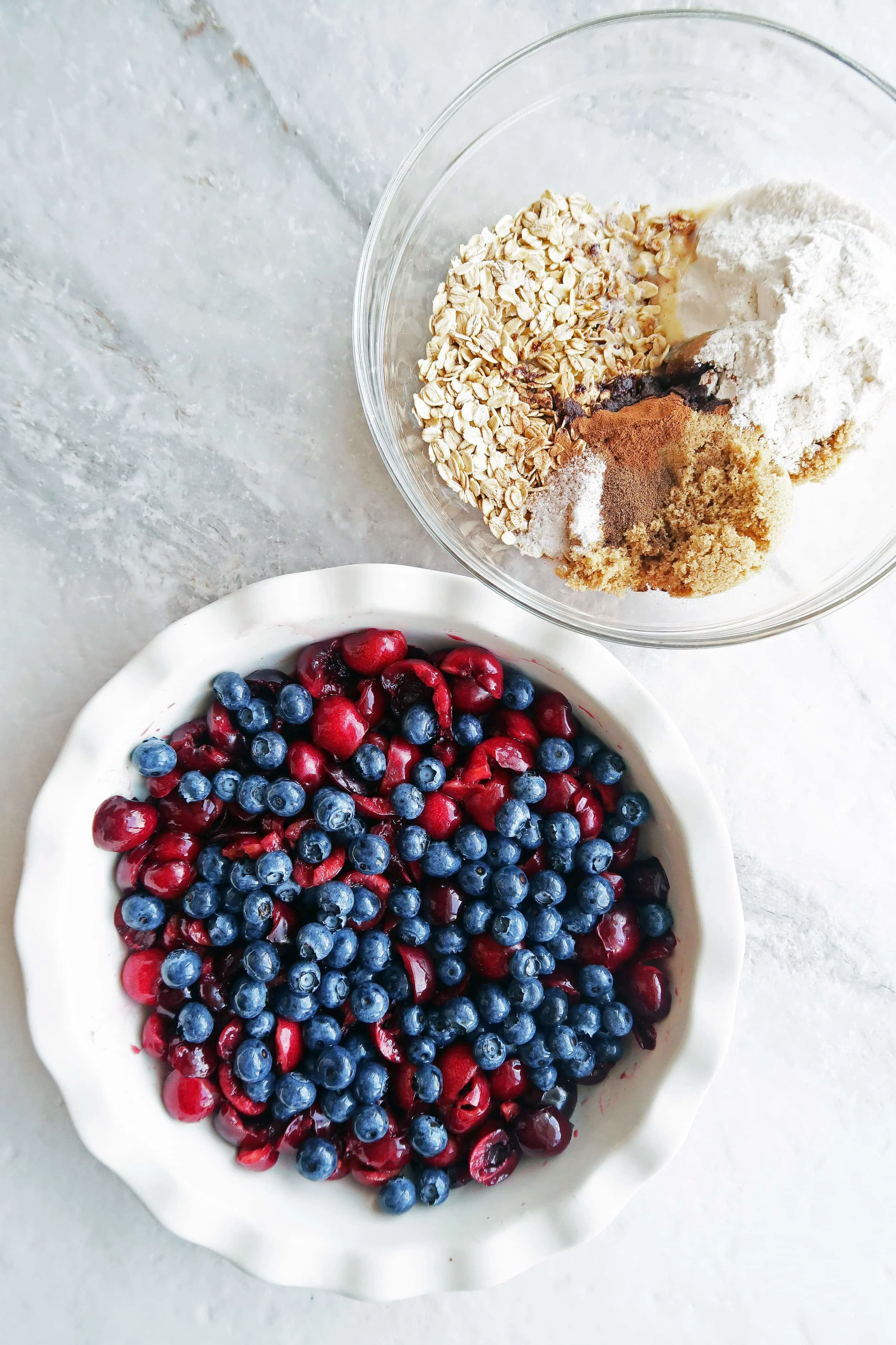 Pitted cherries and blueberries in a pie dish and oats, sugar, flour, and spices in another bowl.
