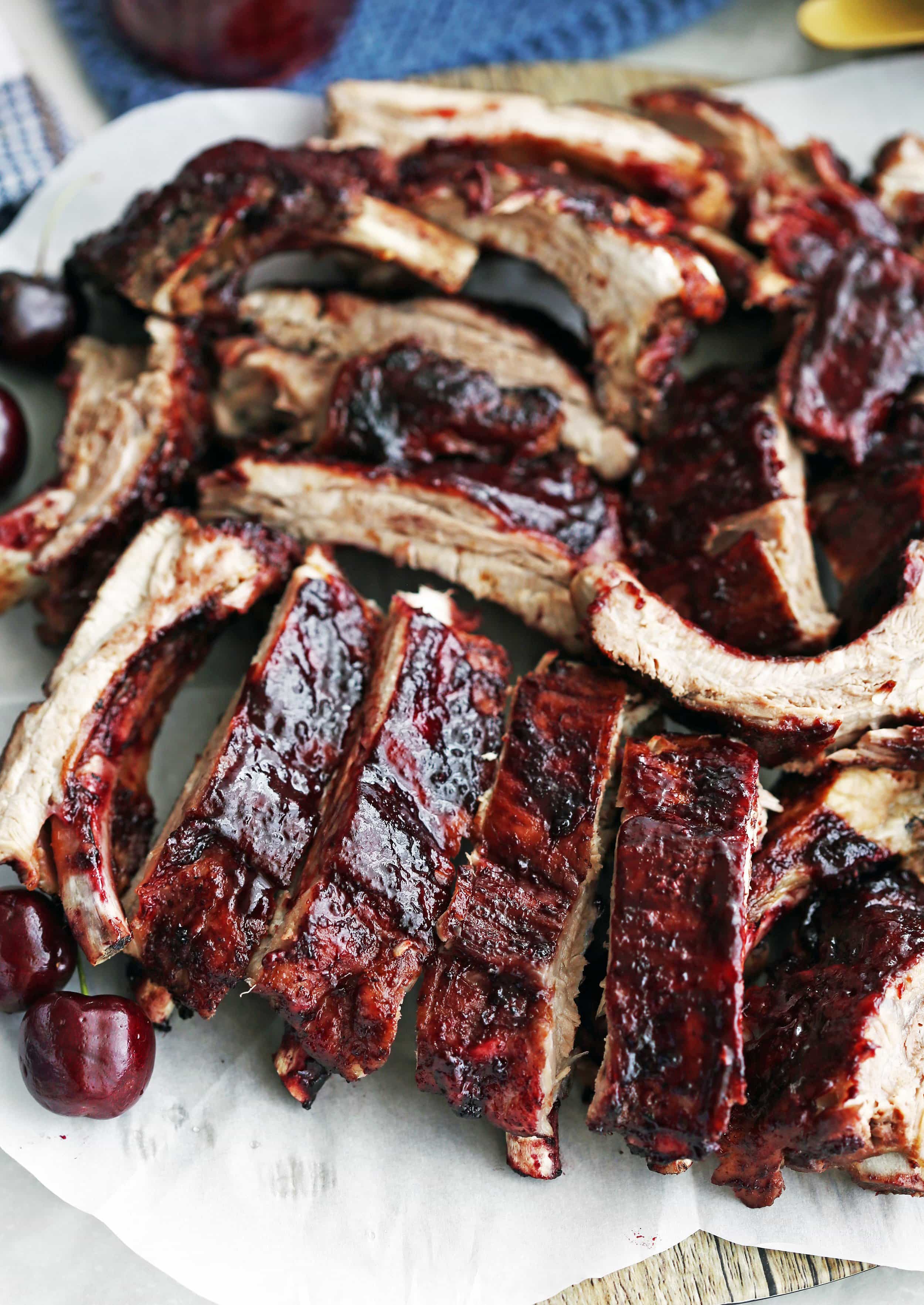 Sliced baby back ribs smothered with cherry chipotle sauce on white parchment paper.