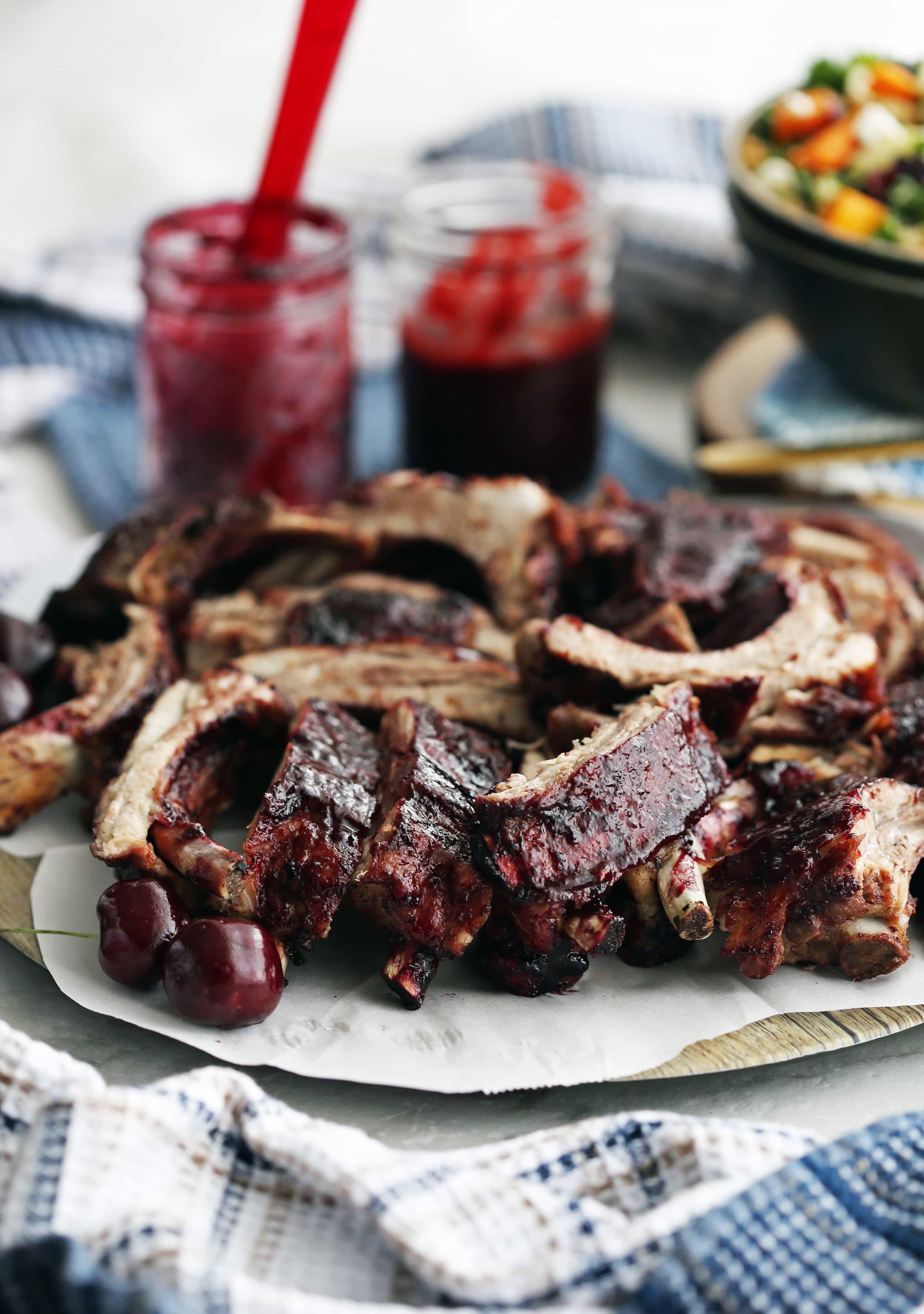 A platter full of pork ribs covered with cherry chipotle sauce with a mason jar of more sauce in the background.