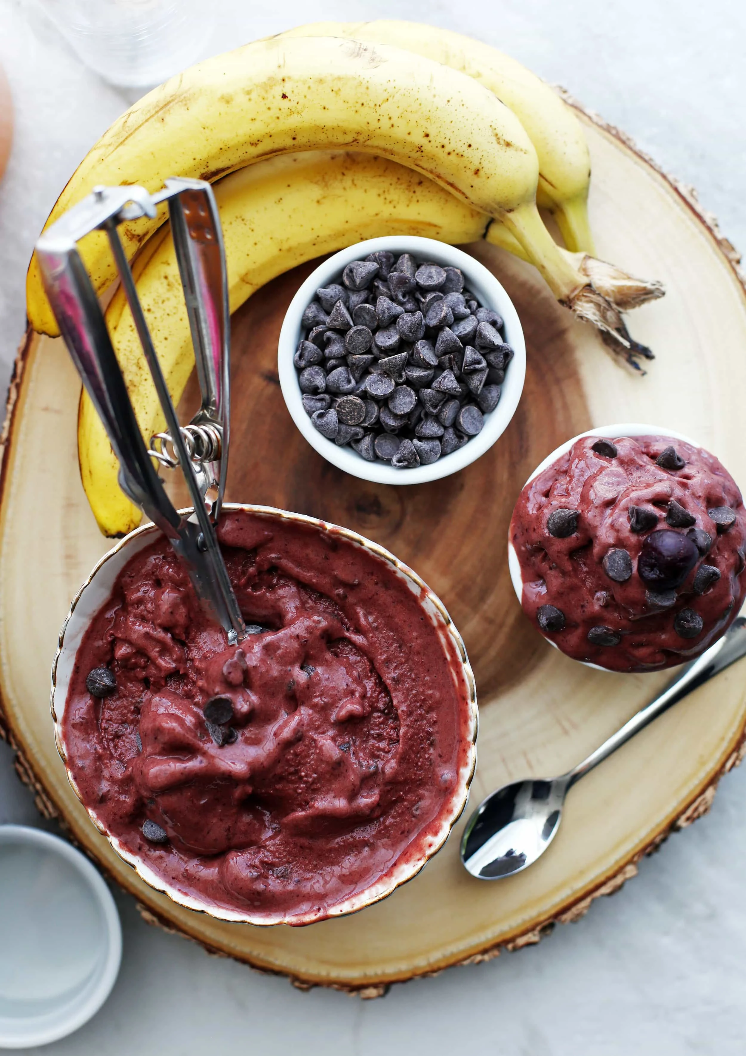 Overhead view of two bowls of cherry chocolate frozen yogurt, a bowl of chocolate chips, and three bananas.