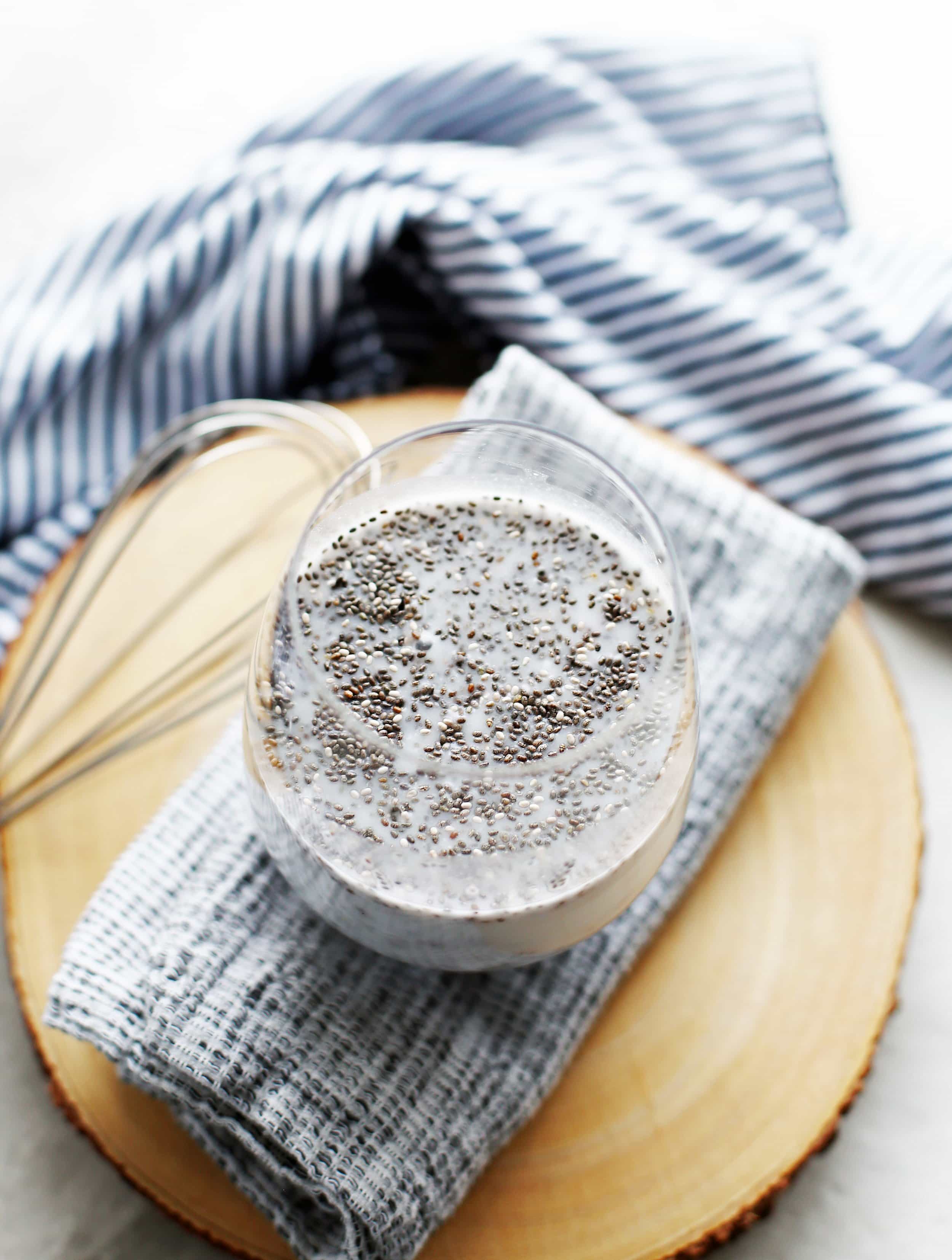 Coconut milk and chia seeds in a round drinking glass with a small whisk to its side.