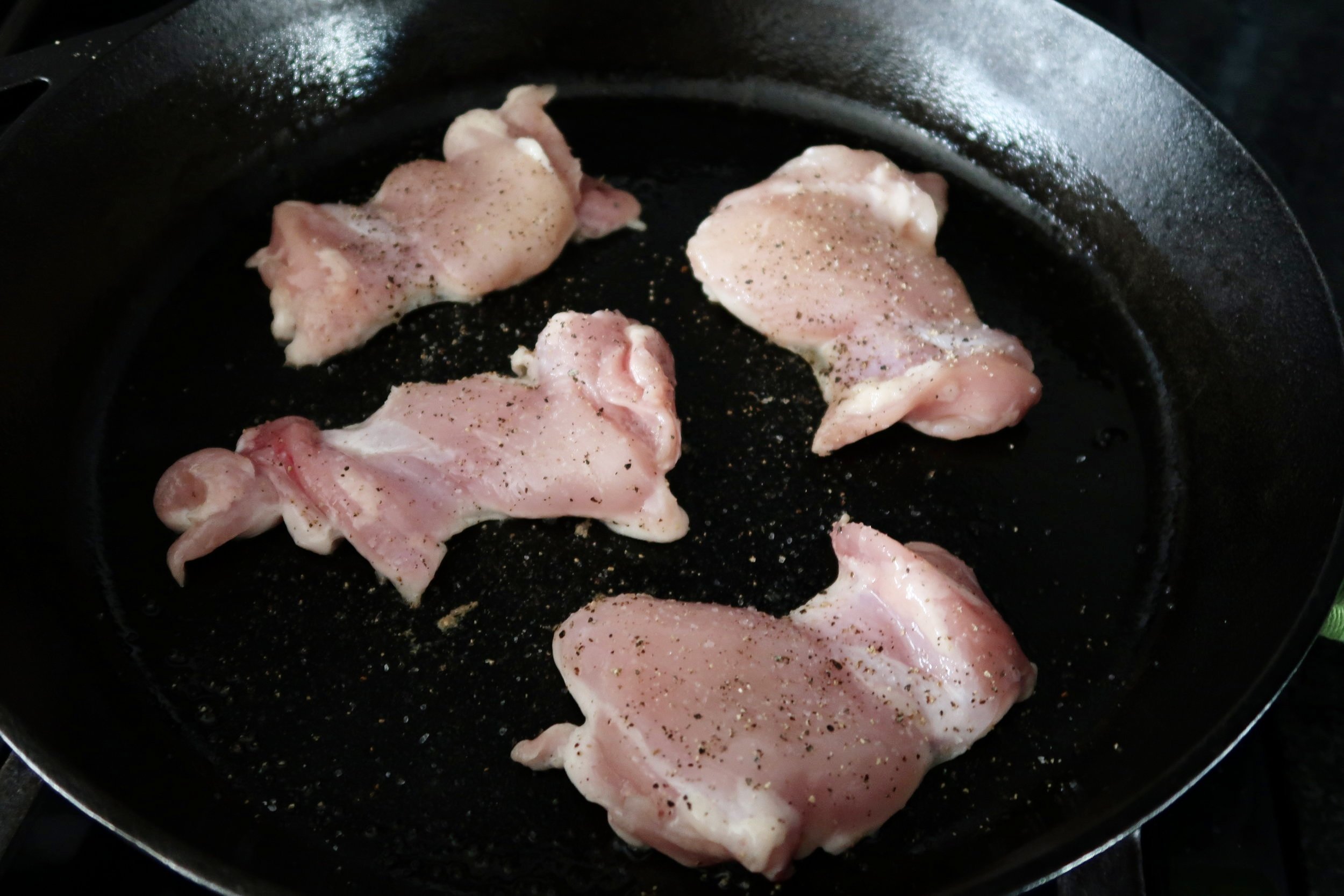 Chicken thighs with salt and pepper cooking in a cast iron skillet.