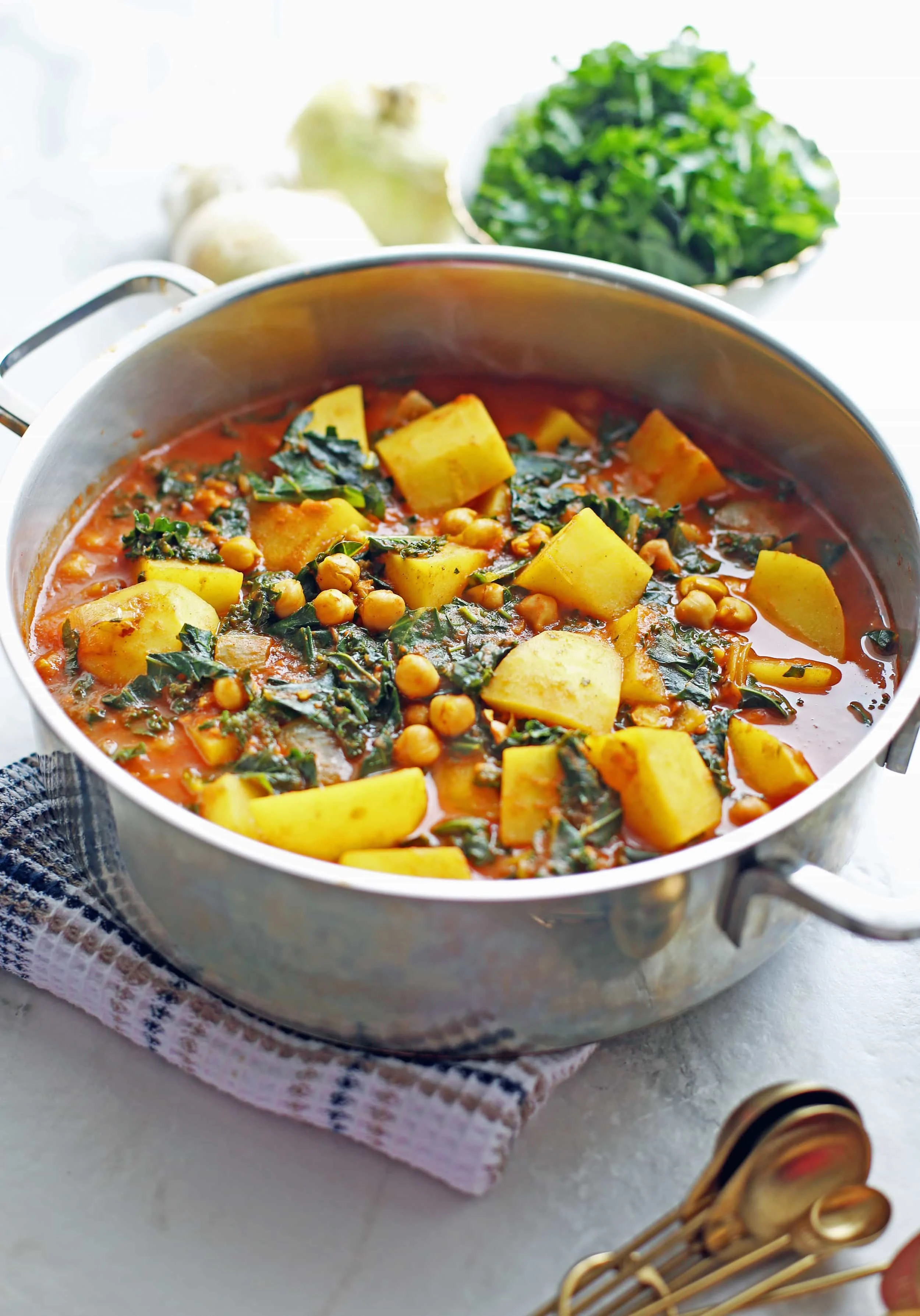 A side view of Spicy Chickpea Kale and Potato Curry in a large silver pot.