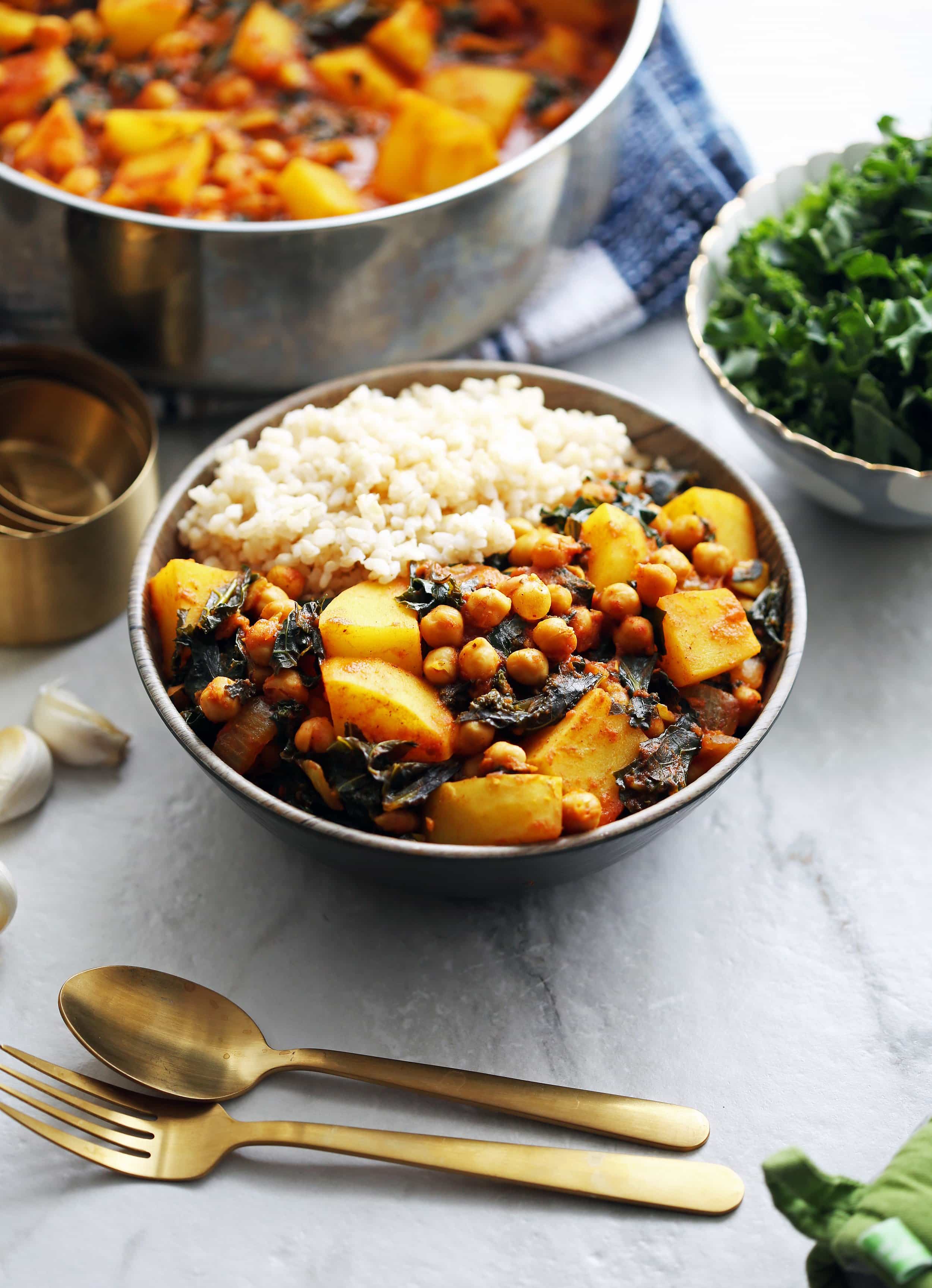 A side angle view of Spicy Chickpea Kale and Potato Curry with rice with a large pot of curry in the background.