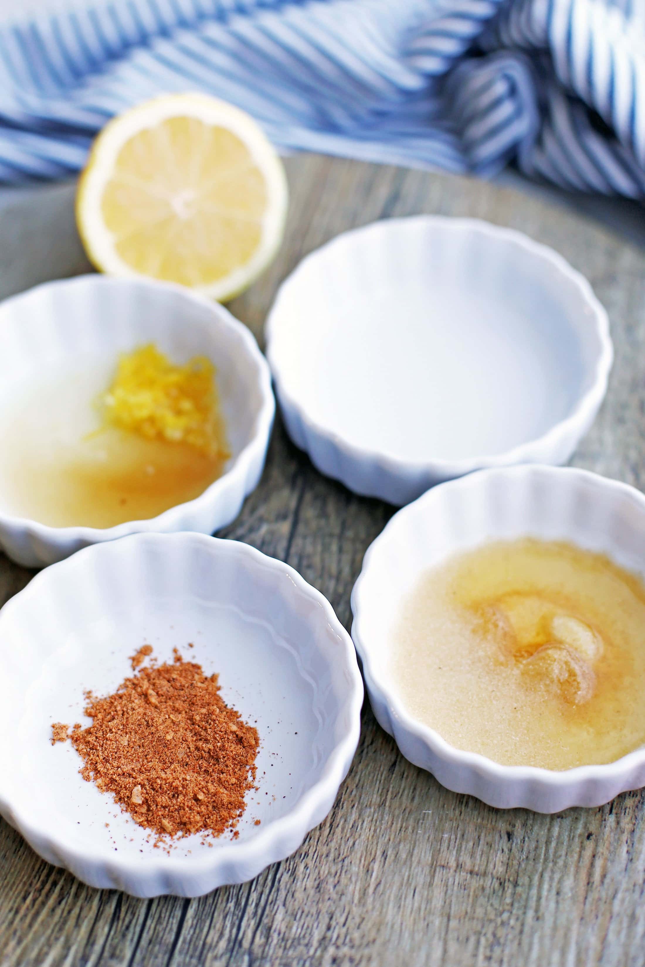 Four mini white tart pans on a round wooden plate containing an assortment of seasonings.