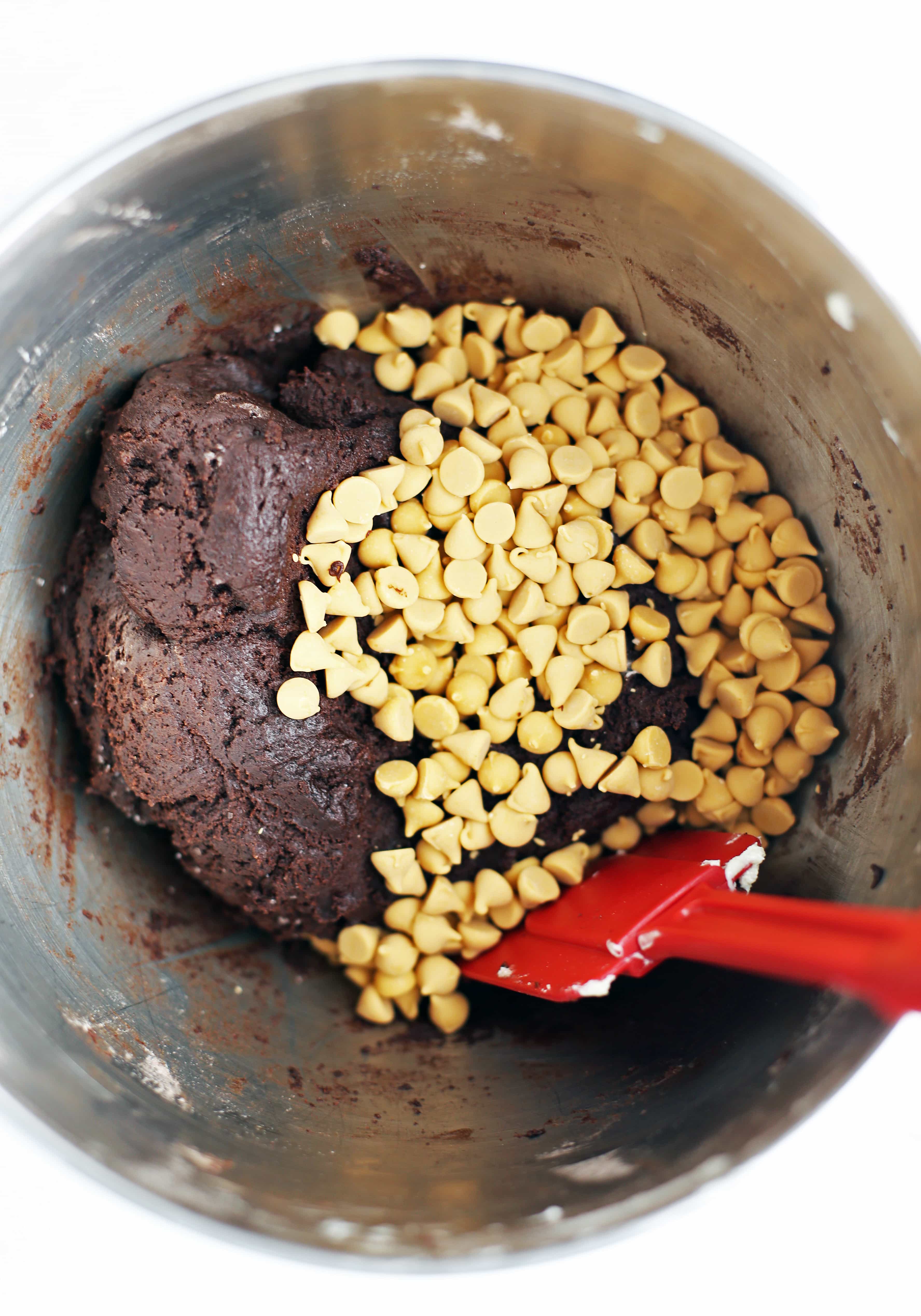 Chocolate cookie batter and butterscotch chips in a stainless steel bowl.