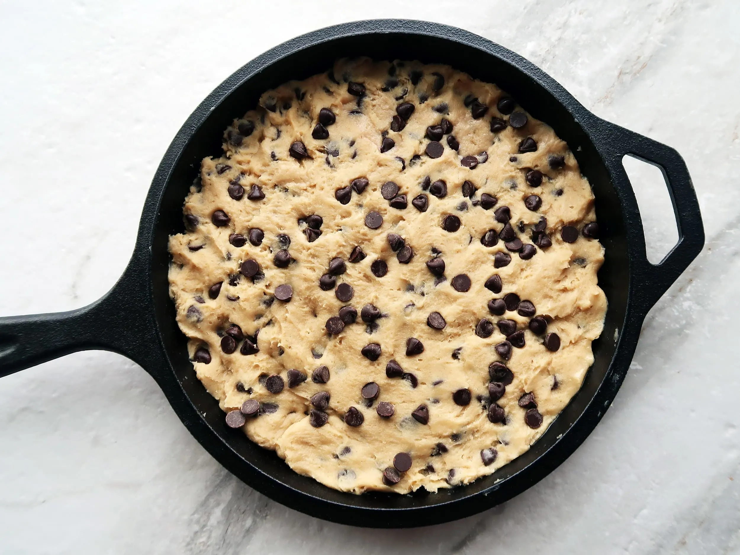 Chocolate chip cookie dough in a cast iron skillet.