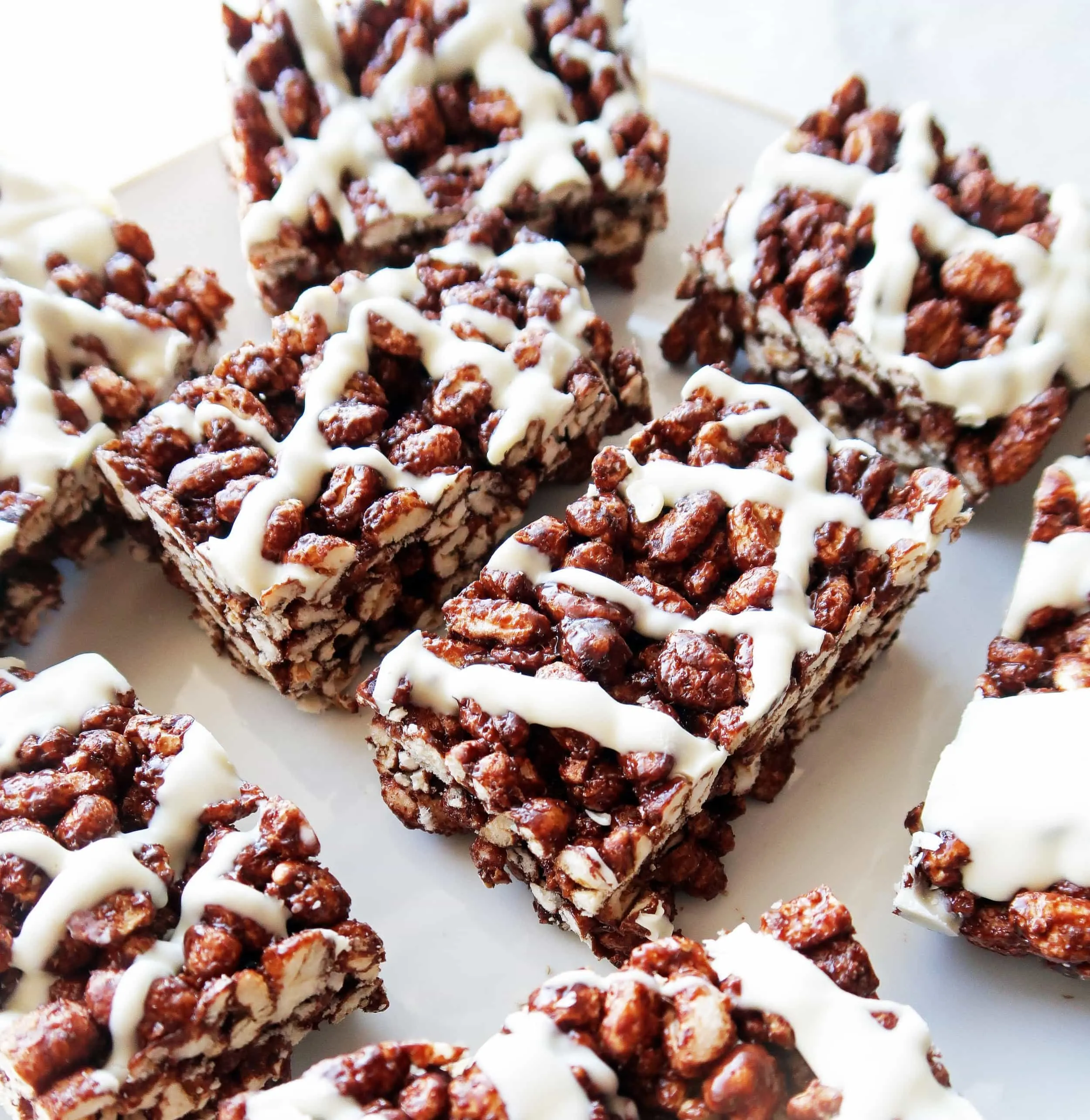 Close up view of Chocolate Marshmallow Puffed Wheat Squares with white chocolate drizzle on a white plate.