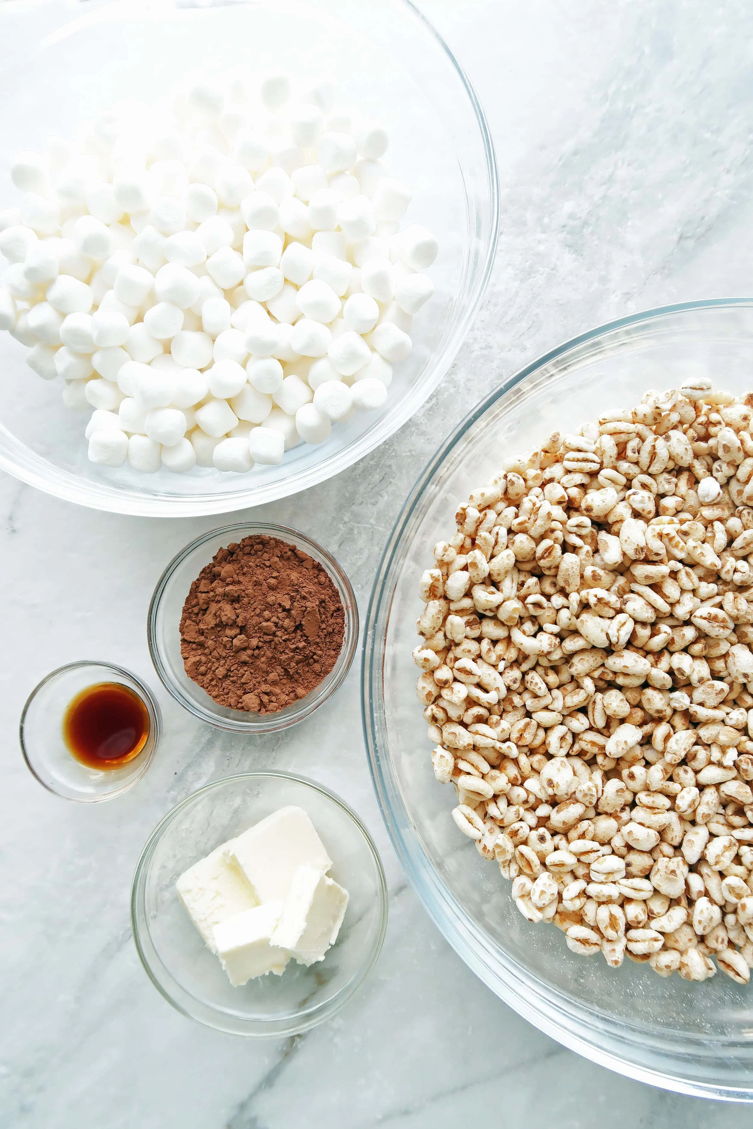 Bowls of puffed wheat, marshmallows, cocoa powder, butter, and vanilla extract.