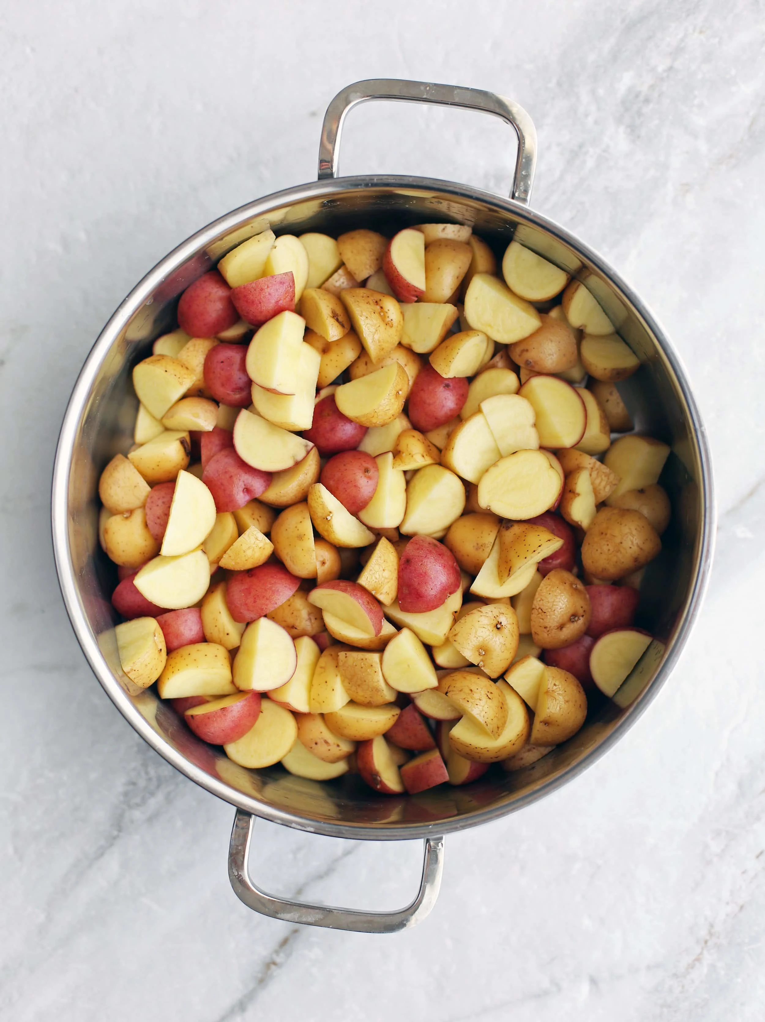 Quartered red and yellow baby potatoes in a large metal pot.