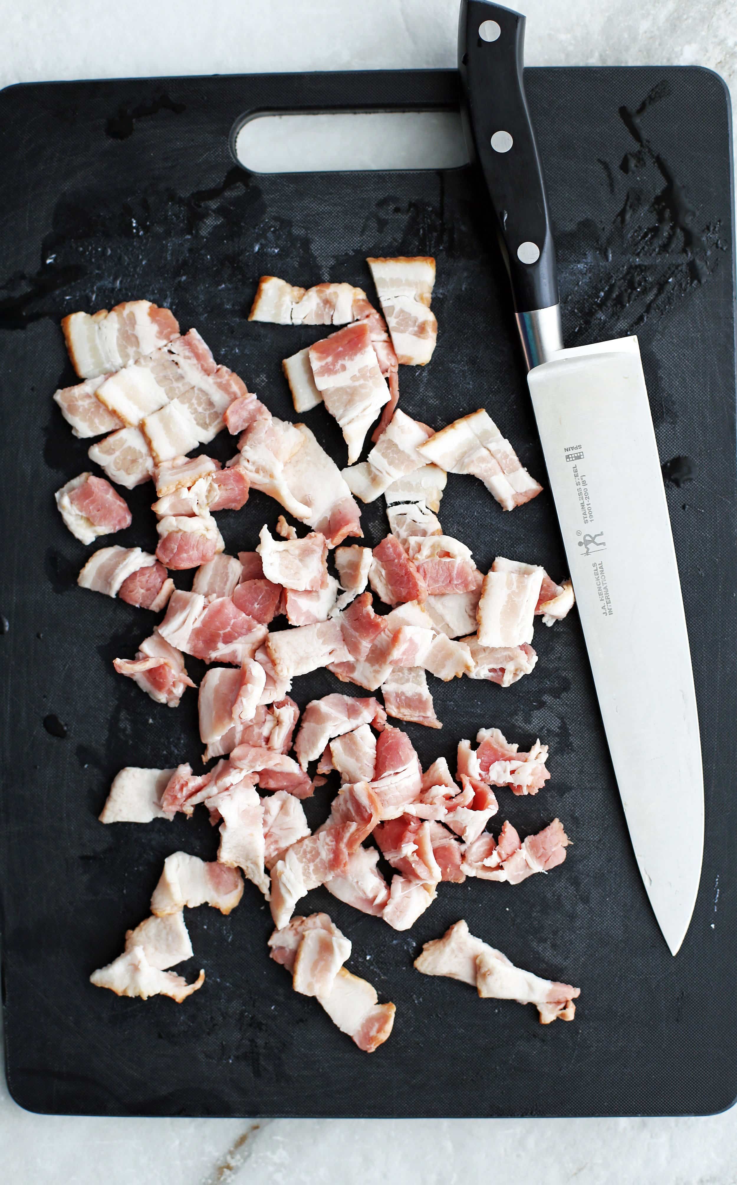 Chopped bacon and knife on a black cutting board.