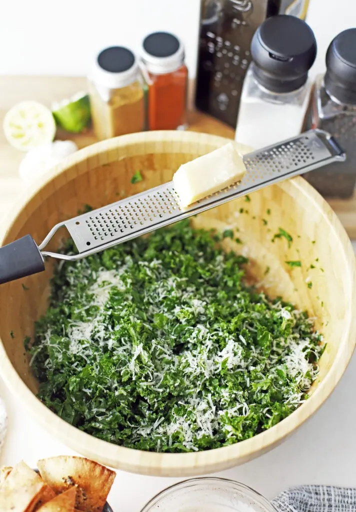 Chopped massaged kale topped with freshly grated parmesan cheese on top in a wooden bowl.