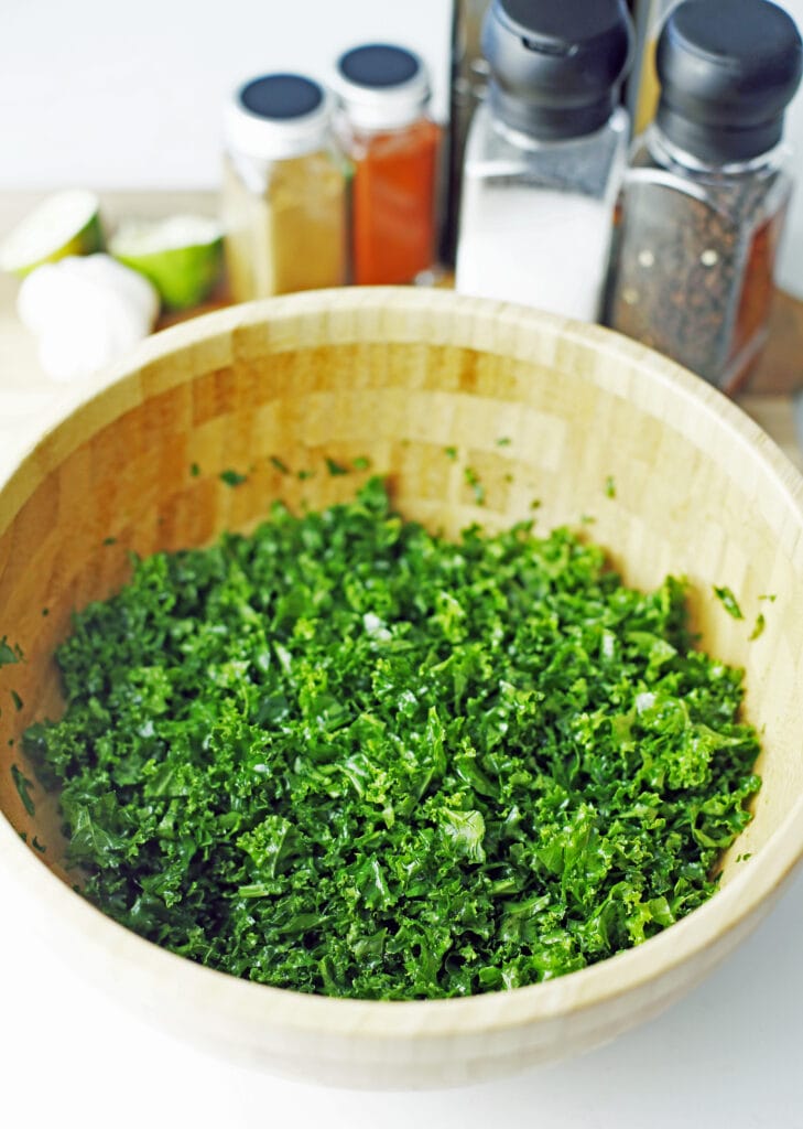 Chopped curly kale with olive oil, salt, and pepper in a large wooden bowl.