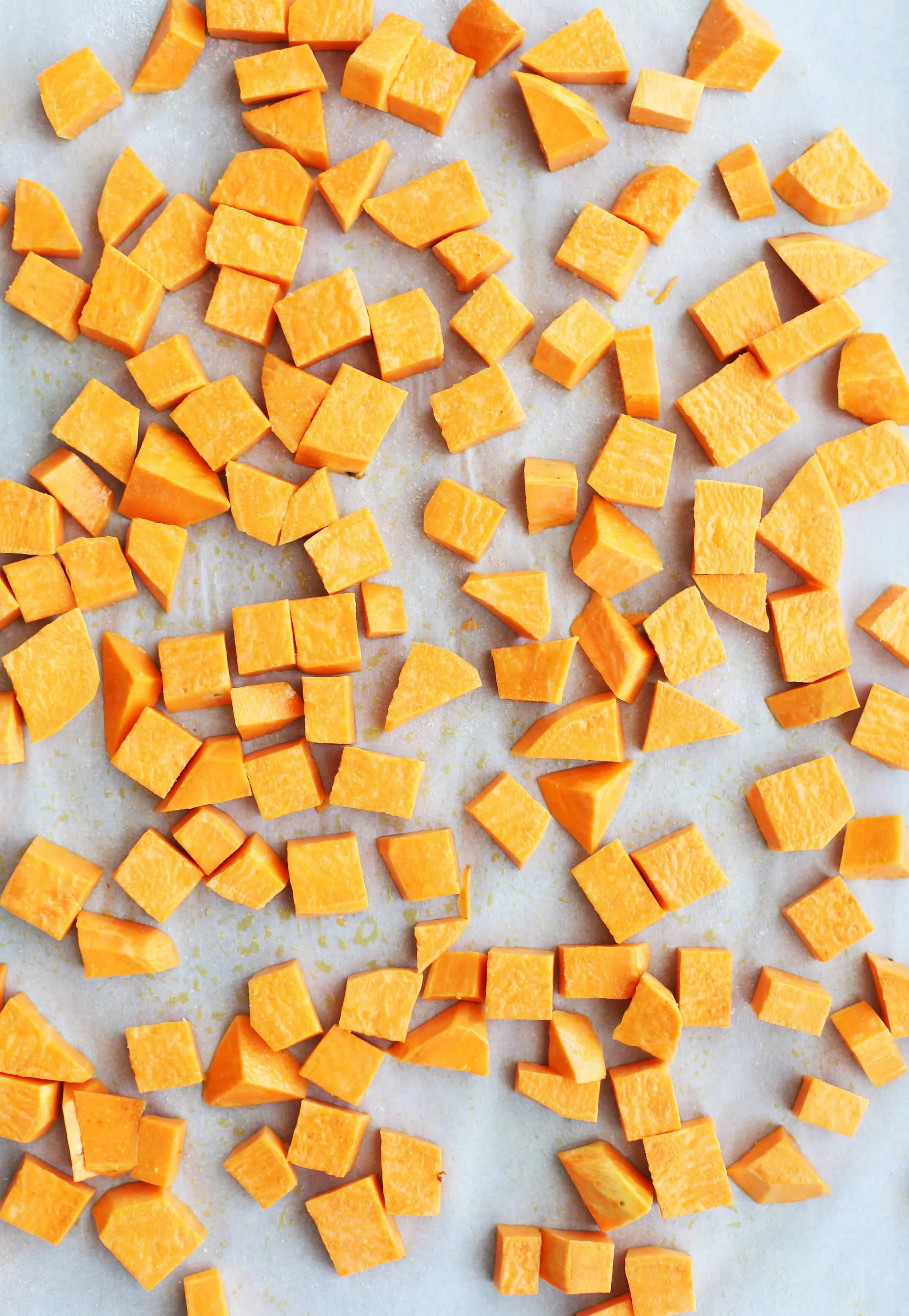 Peeled and chopped sweet potatoes on a baking sheet lined with parchment paper.