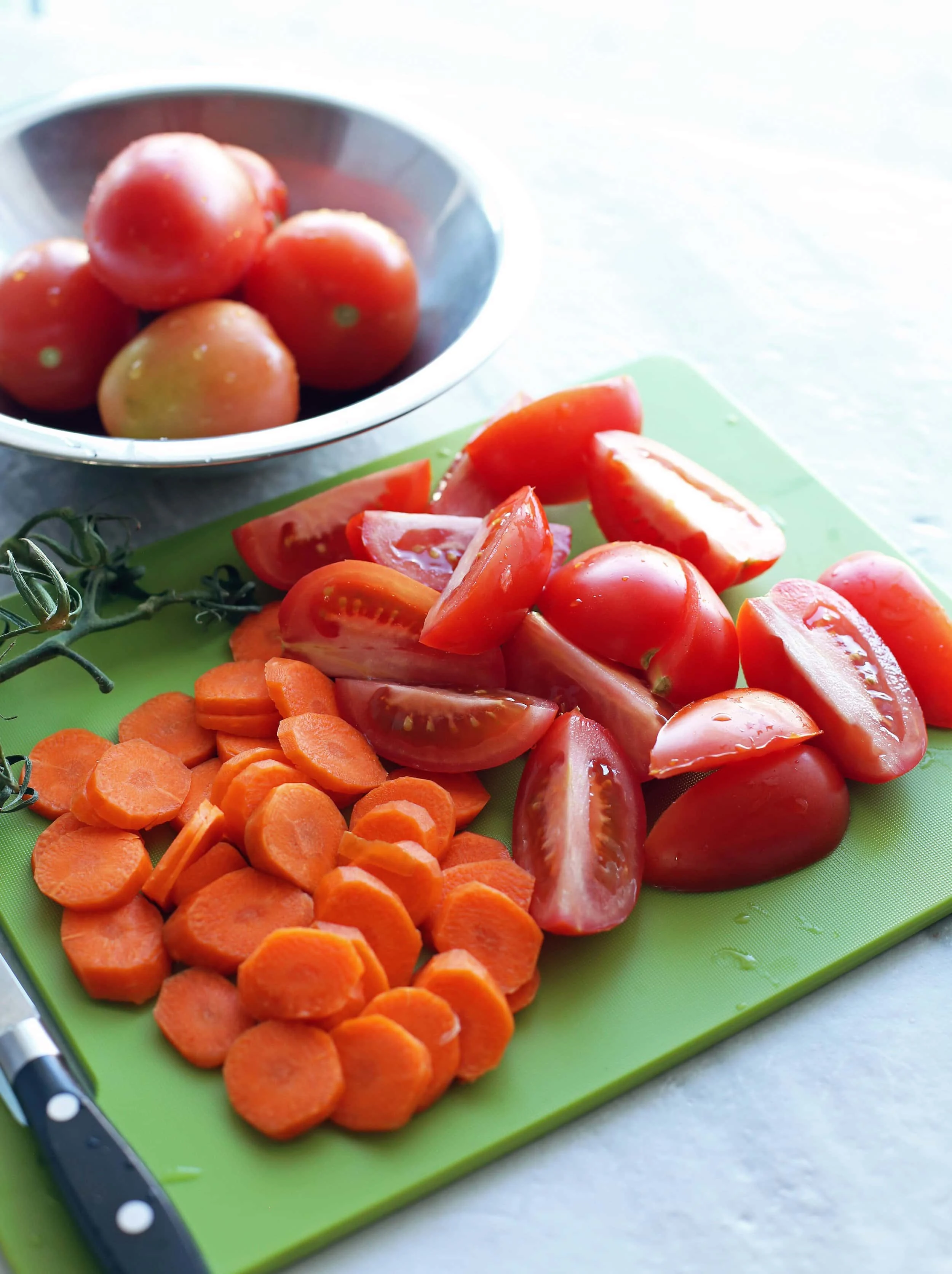 Chopped carrots and quartered Roma tomatoes on a green cutting board.
