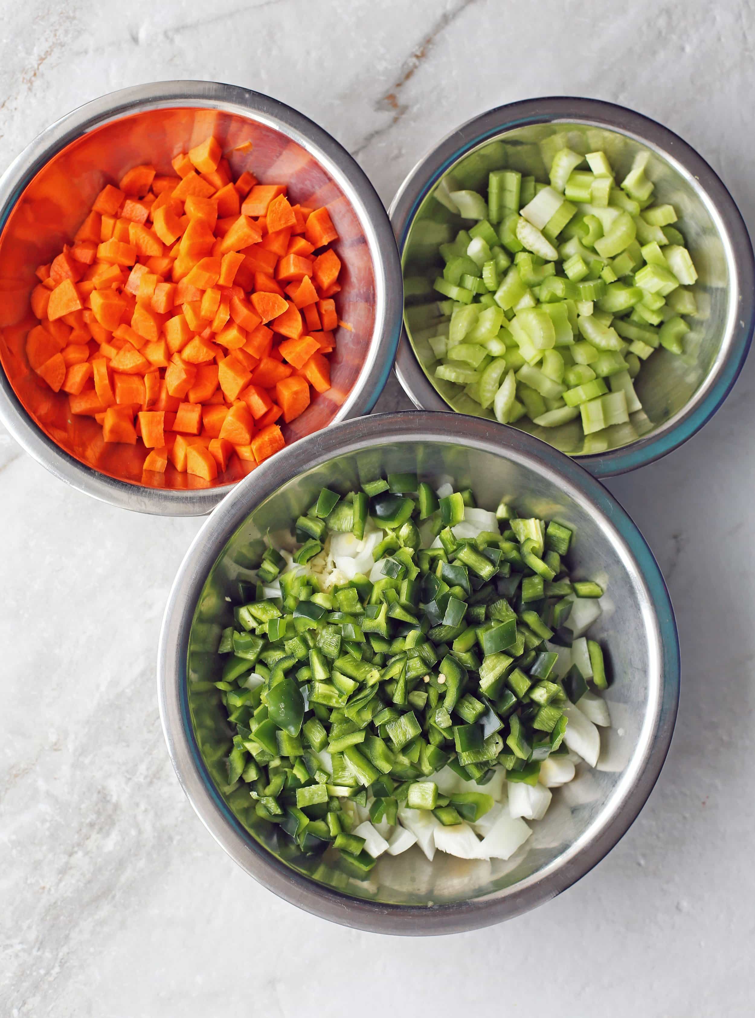 Three metal bowls containing diced peppers, onions, carrots, and celery.