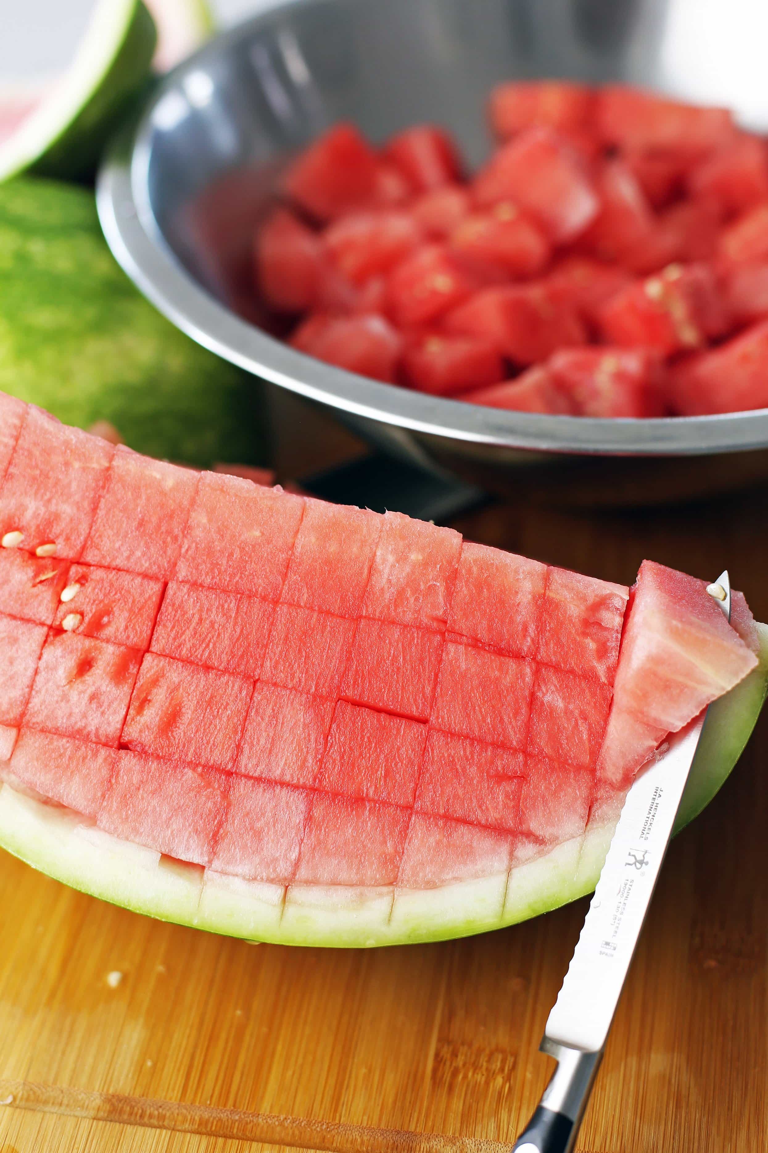 A quarter seedless watermelon with knife cuts in it with a serrated knife cutting into it.