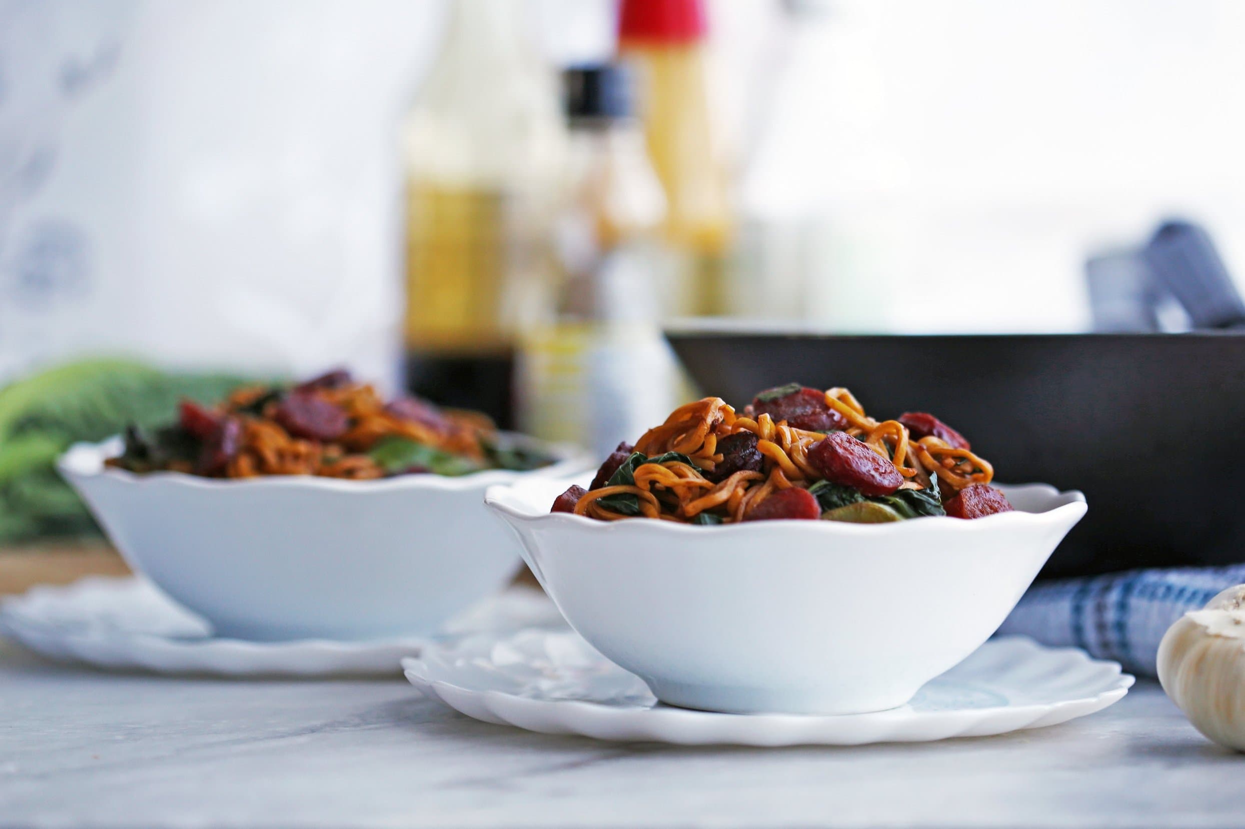 Side view of two bowls of A bowl of lo mein noodles with Chinese sausage (lap cheong) and Chinese broccoli (Gai lan).