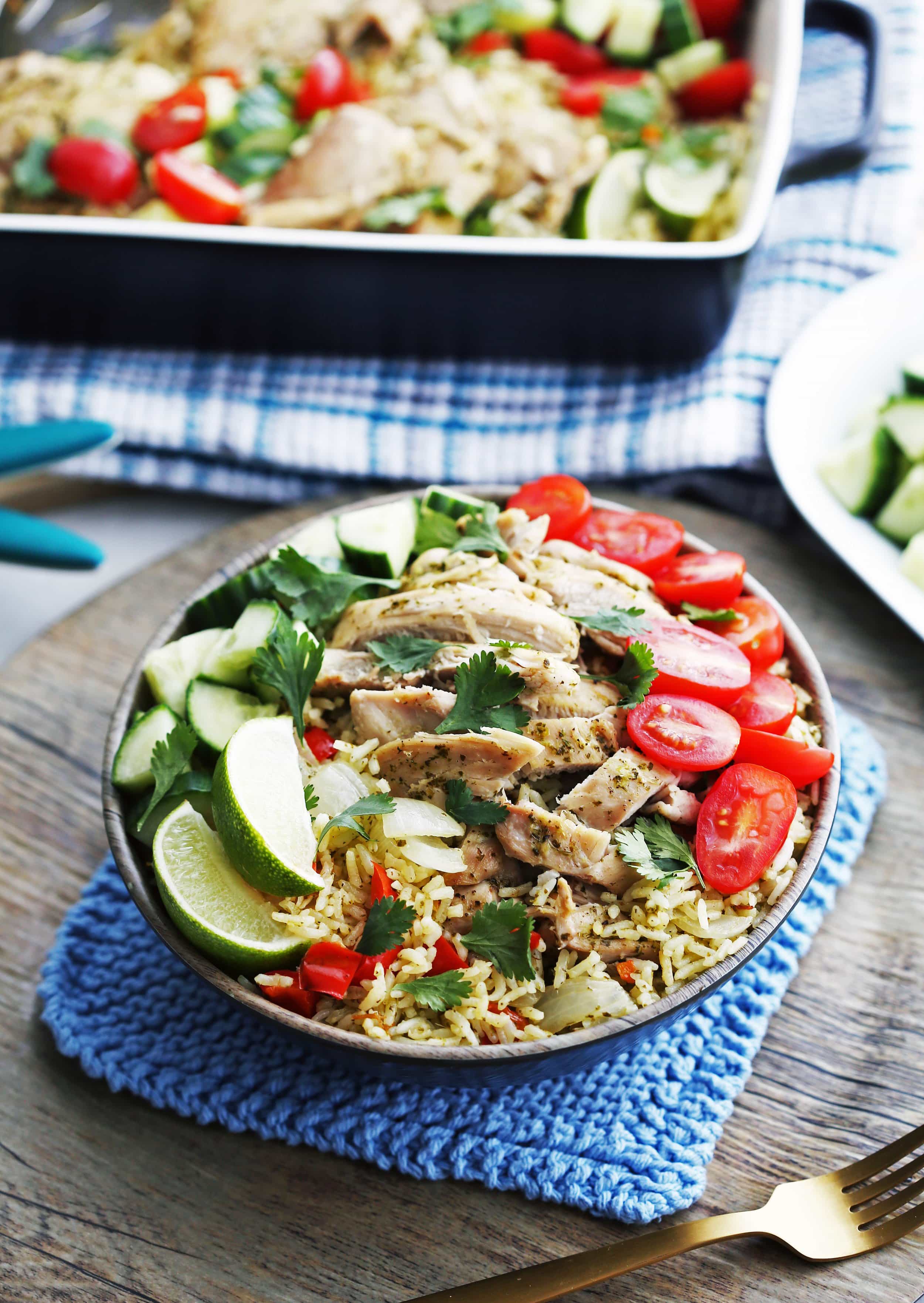 Cilantro Lime Chicken and Rice with tomatoes, cucumbers, cilantro, and lime wedges in a wooden bowl.