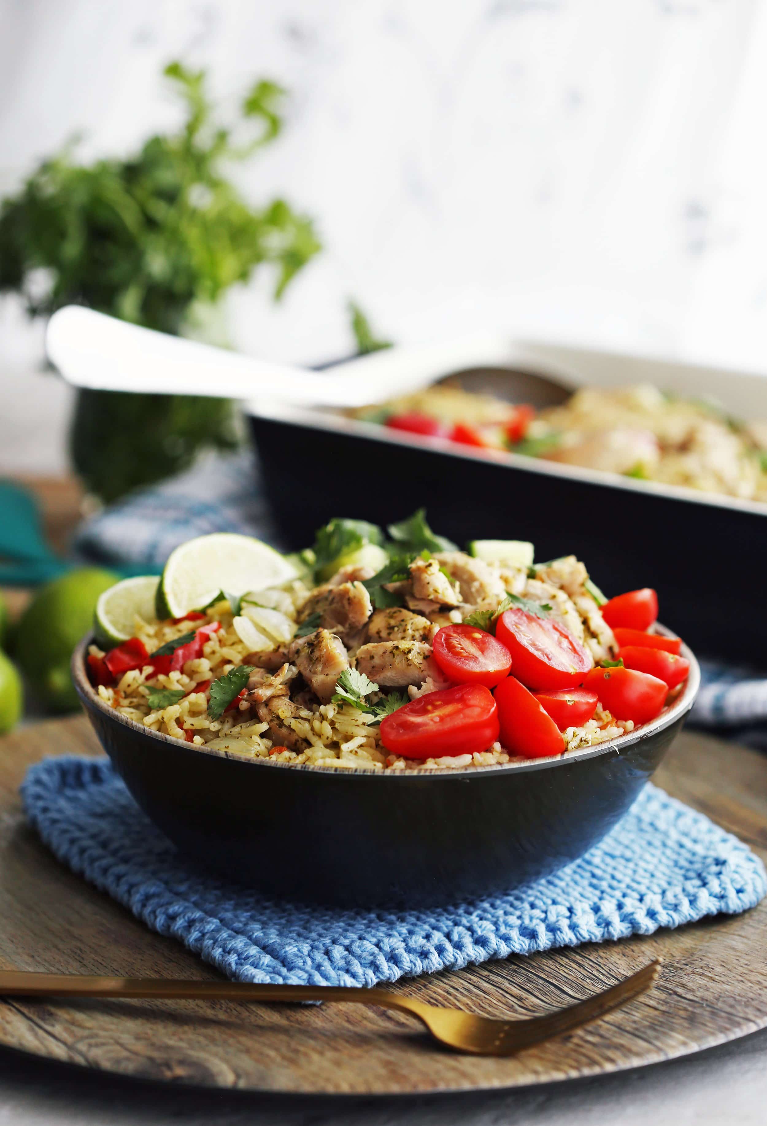 A wooden bowl full of cilantro lime chicken and rice with tomatoes, cucumbers, lime wedges, and fresh cilantro.