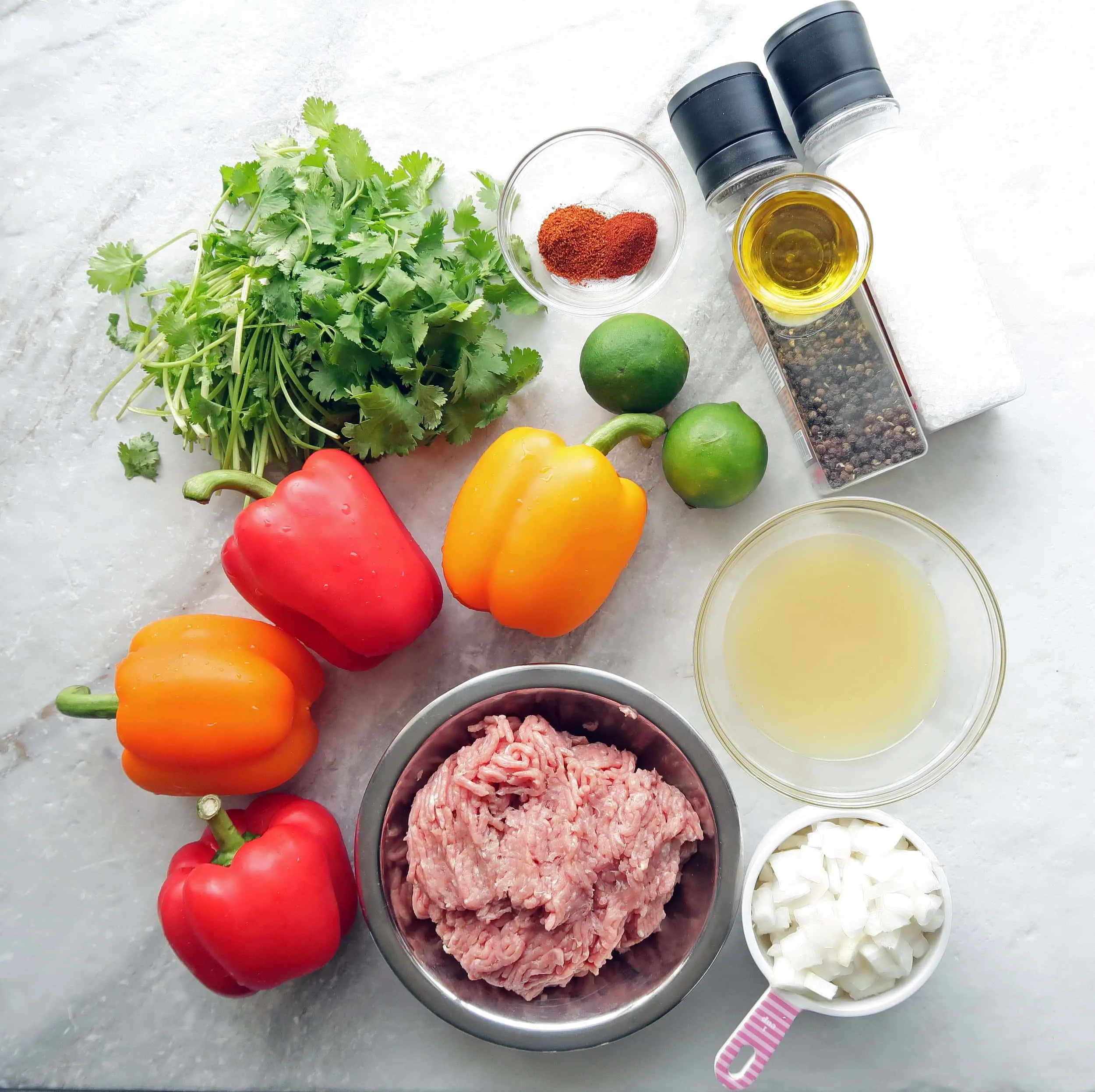 On overhead view of ground turkey, chopped onions, red and yellow bell peppers, fresh cilantro,limes, and spices.