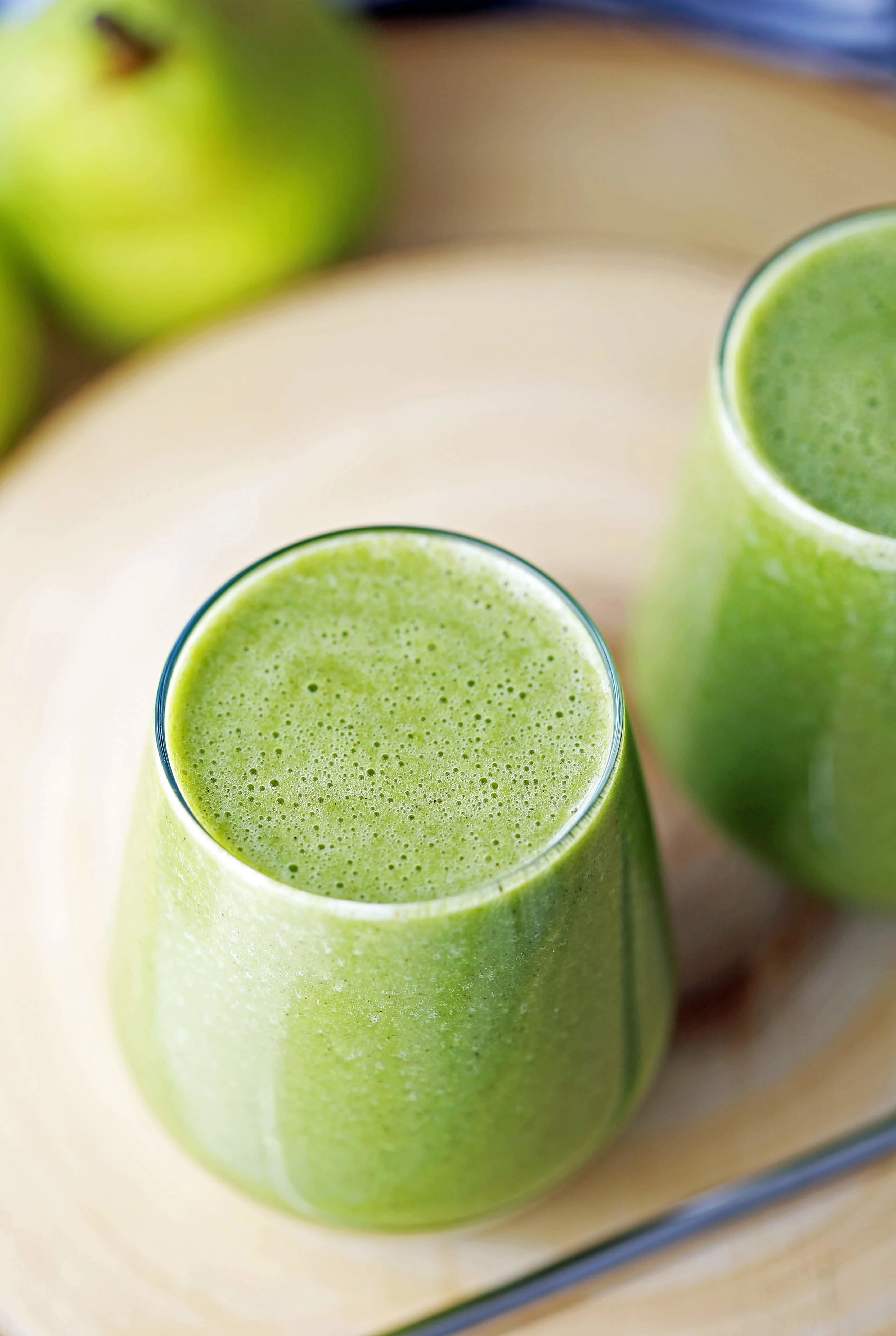 A close-up top view of a full glass of green smoothie made with pears, spinach, ground cinnamon, and almond milk.