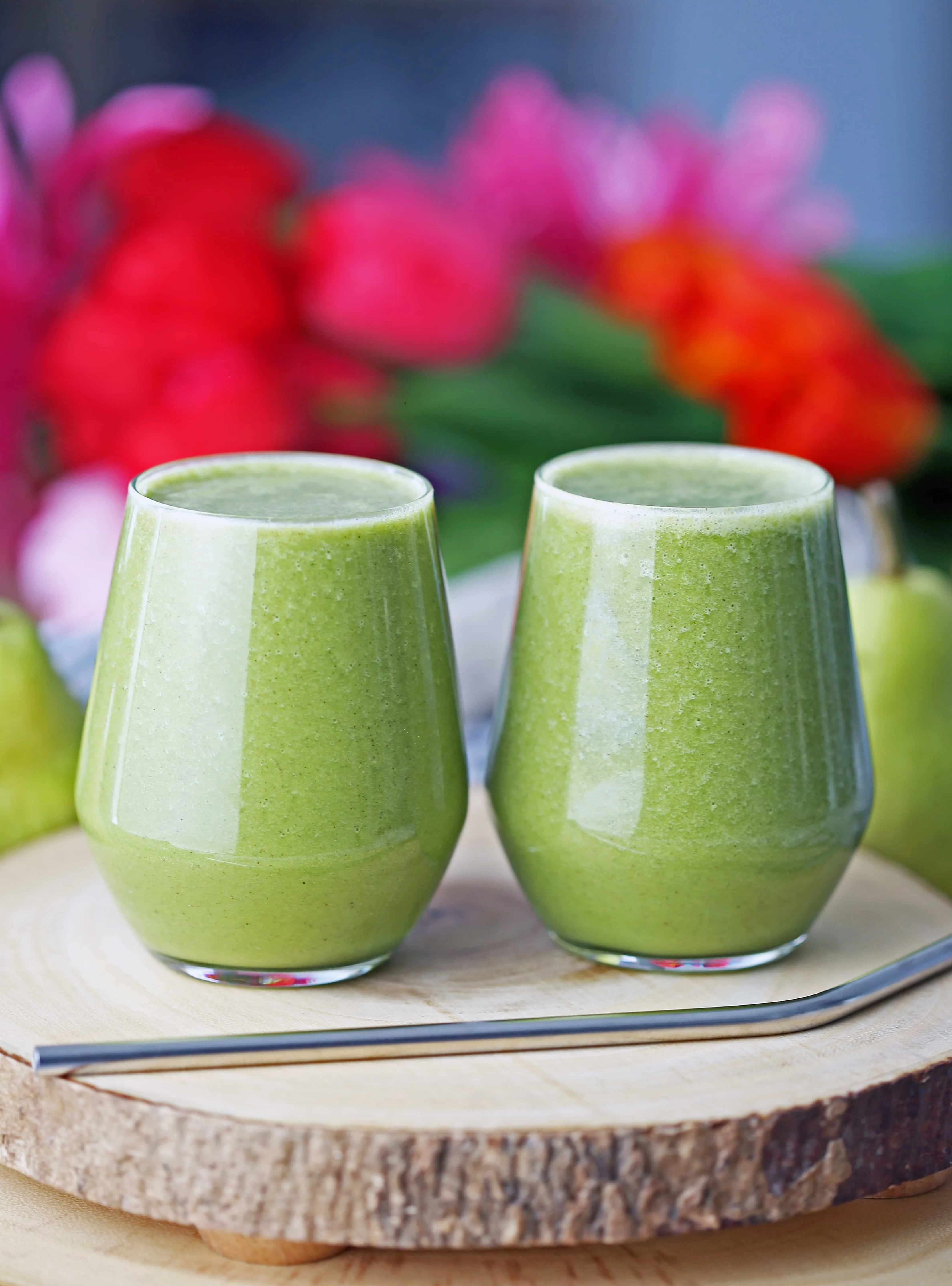 Cinnamon pear green smoothie in two glasses side by side on a wooden board. 