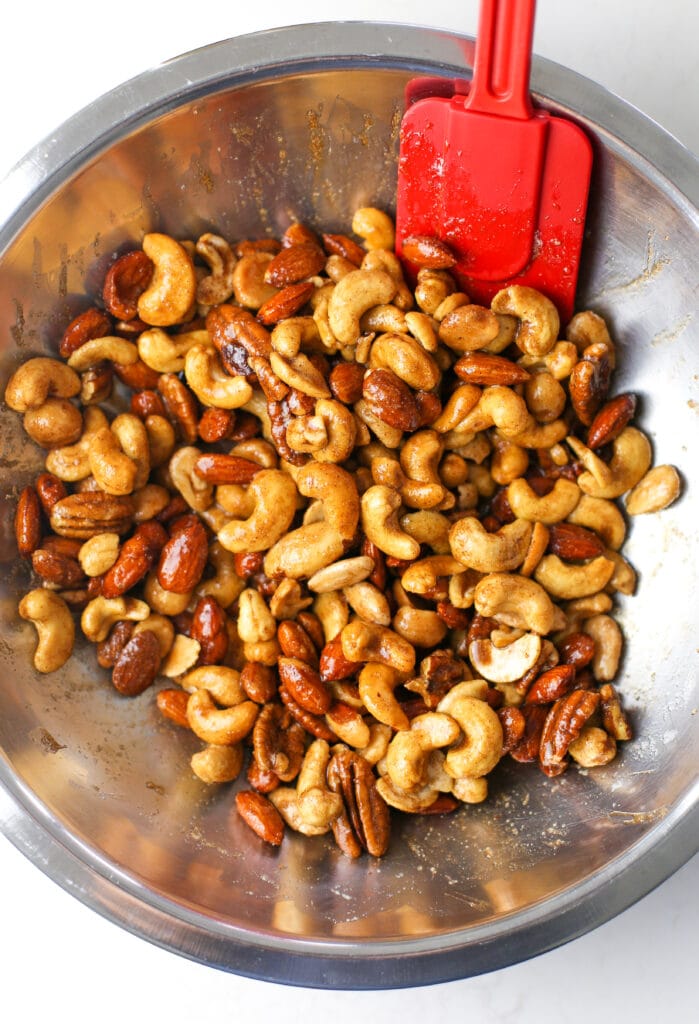 Mixed nuts mixed in a cinnamon sugar sauce in a stainless steel bowl.