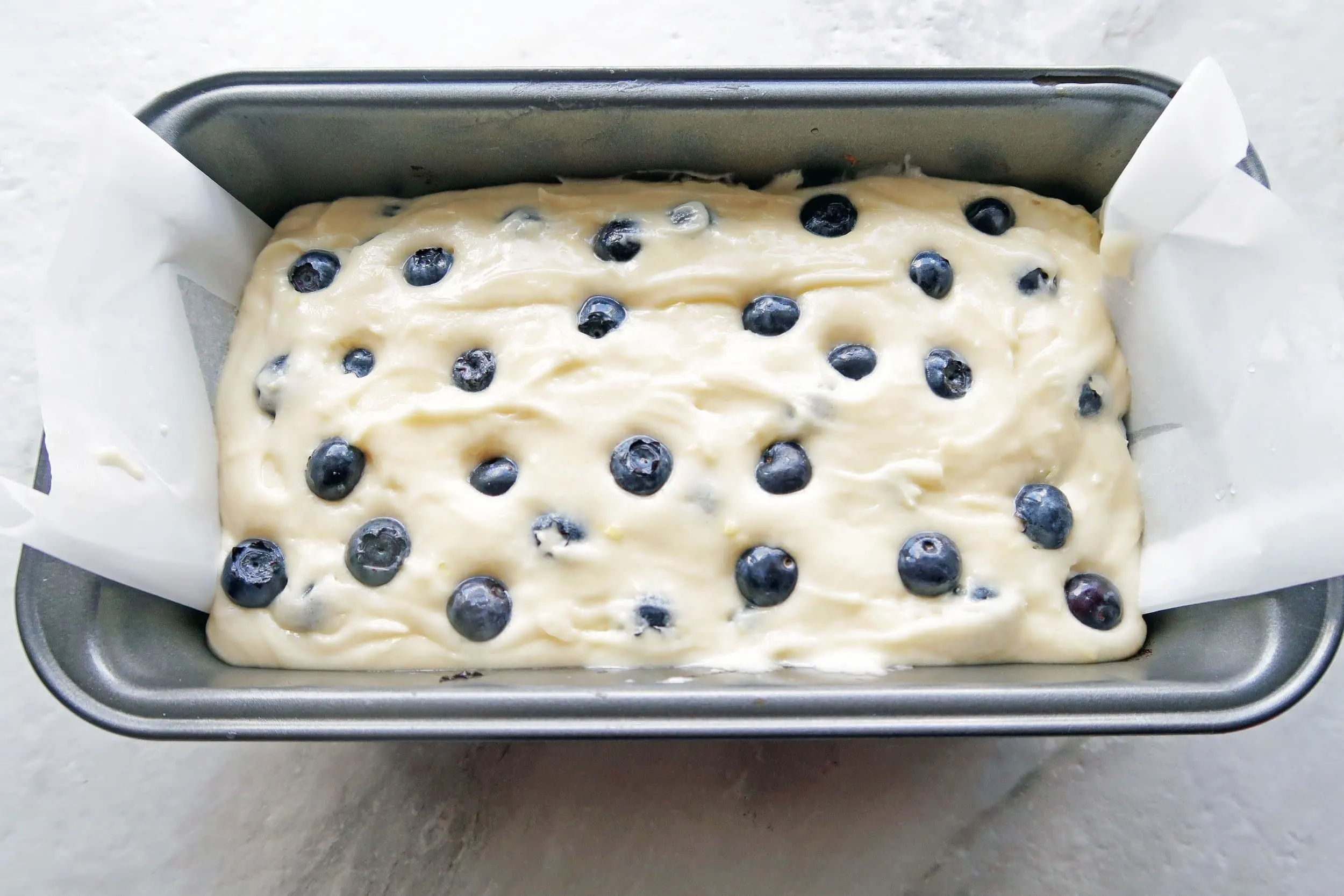 Lemon blueberry loaf cake batter in a loaf pan with more blueberries on top, ready for the oven.