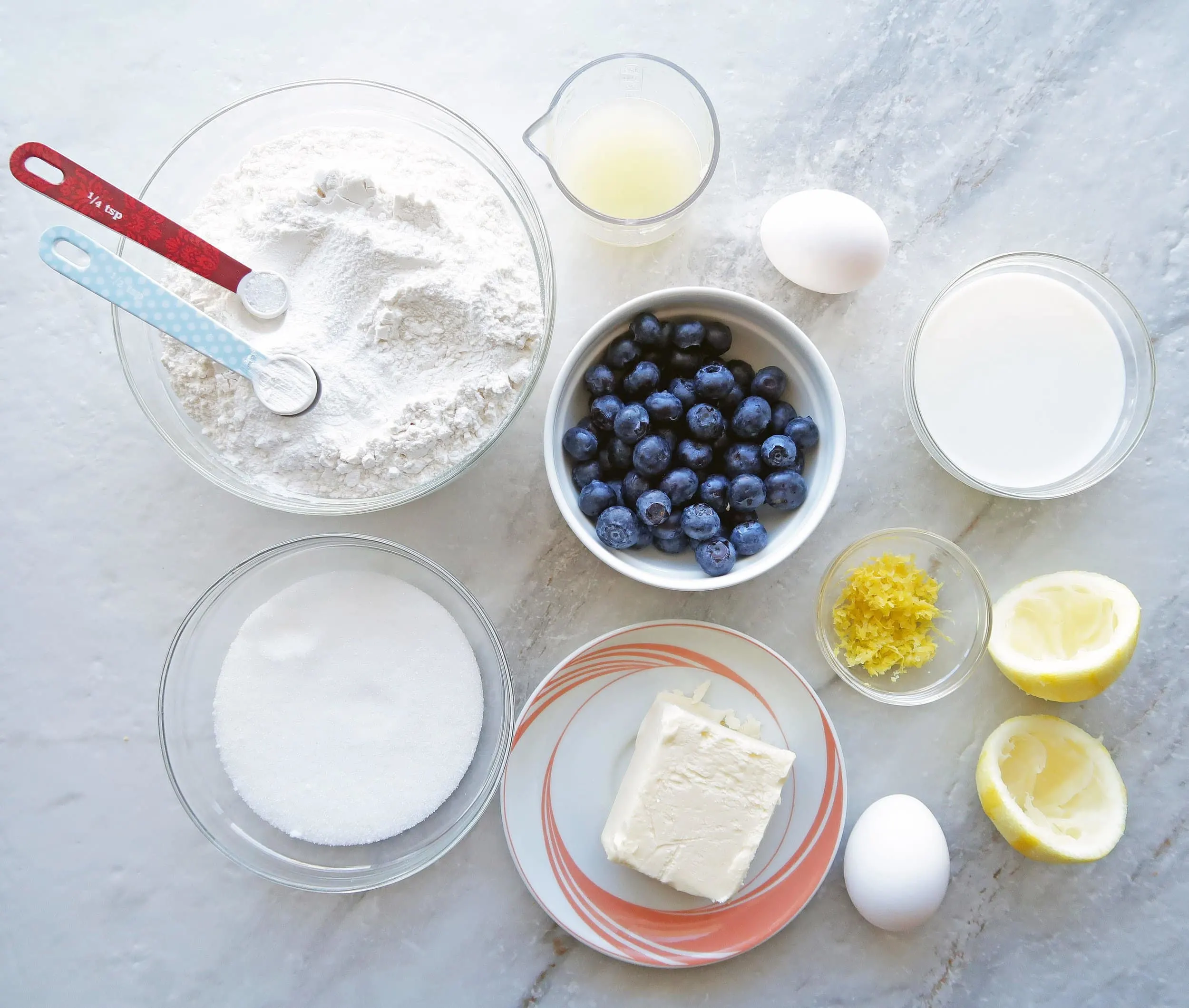 Bowls of blueberries, lemon zest, lemon juice, flour, butter, sugar, milk, and eggs.