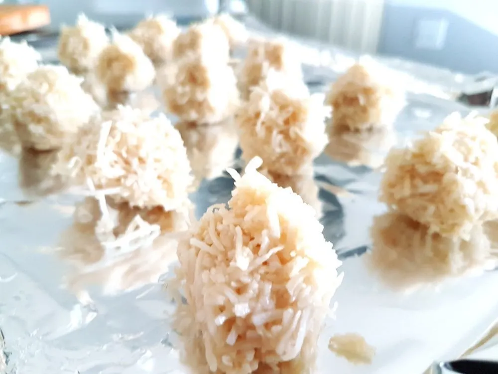 Coconut balls coated with chocolate on a baking sheet.