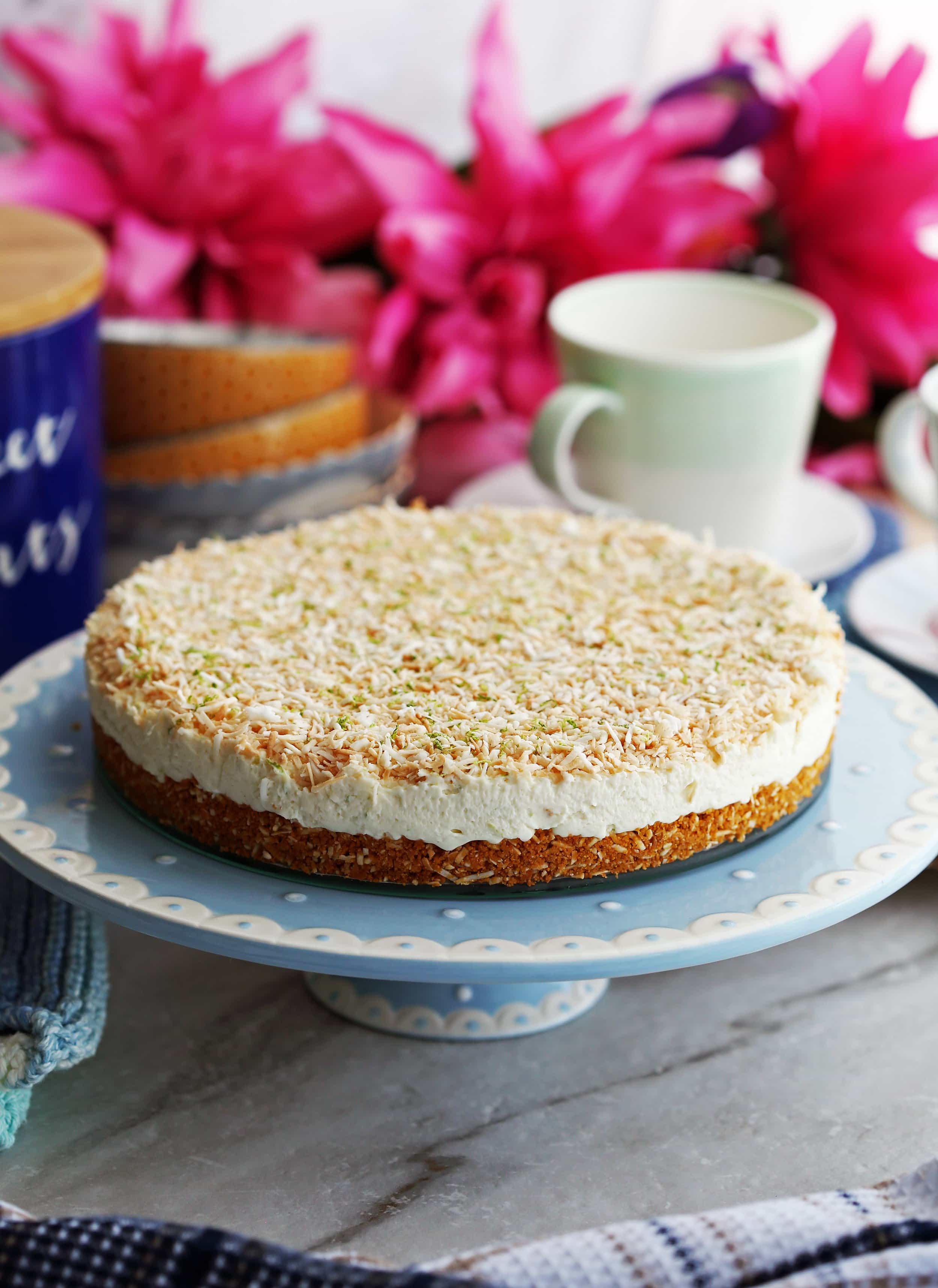 A whole uncut no-bake coconut lime mascarpone cheesecake on a elevated blue cake platter.