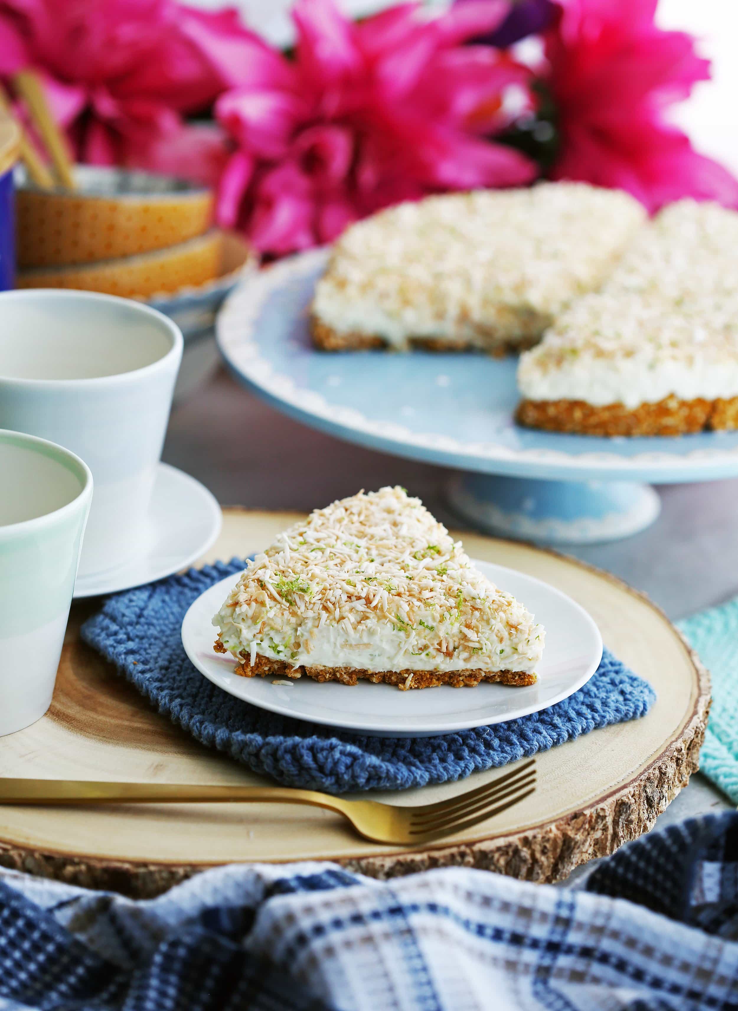 A slice of no-bake coconut lime mascarpone cheesecake on a white plate with more cheesecake on a cake platter behind it.