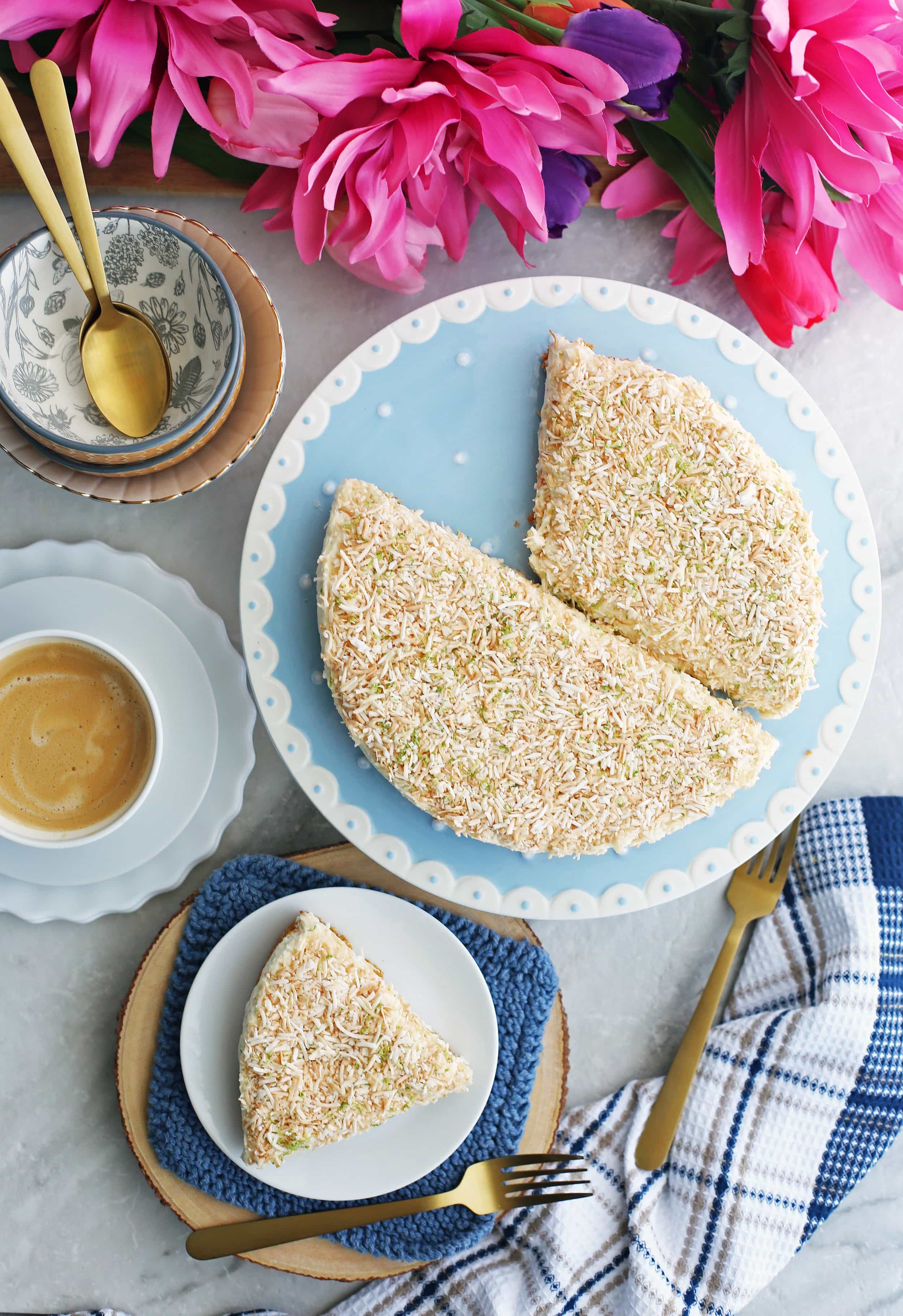 Overhead view of a plate with a slice of no-bake coconut lime mascarpone cheesecake and a blue cake platter with the rest of the cheesecake.