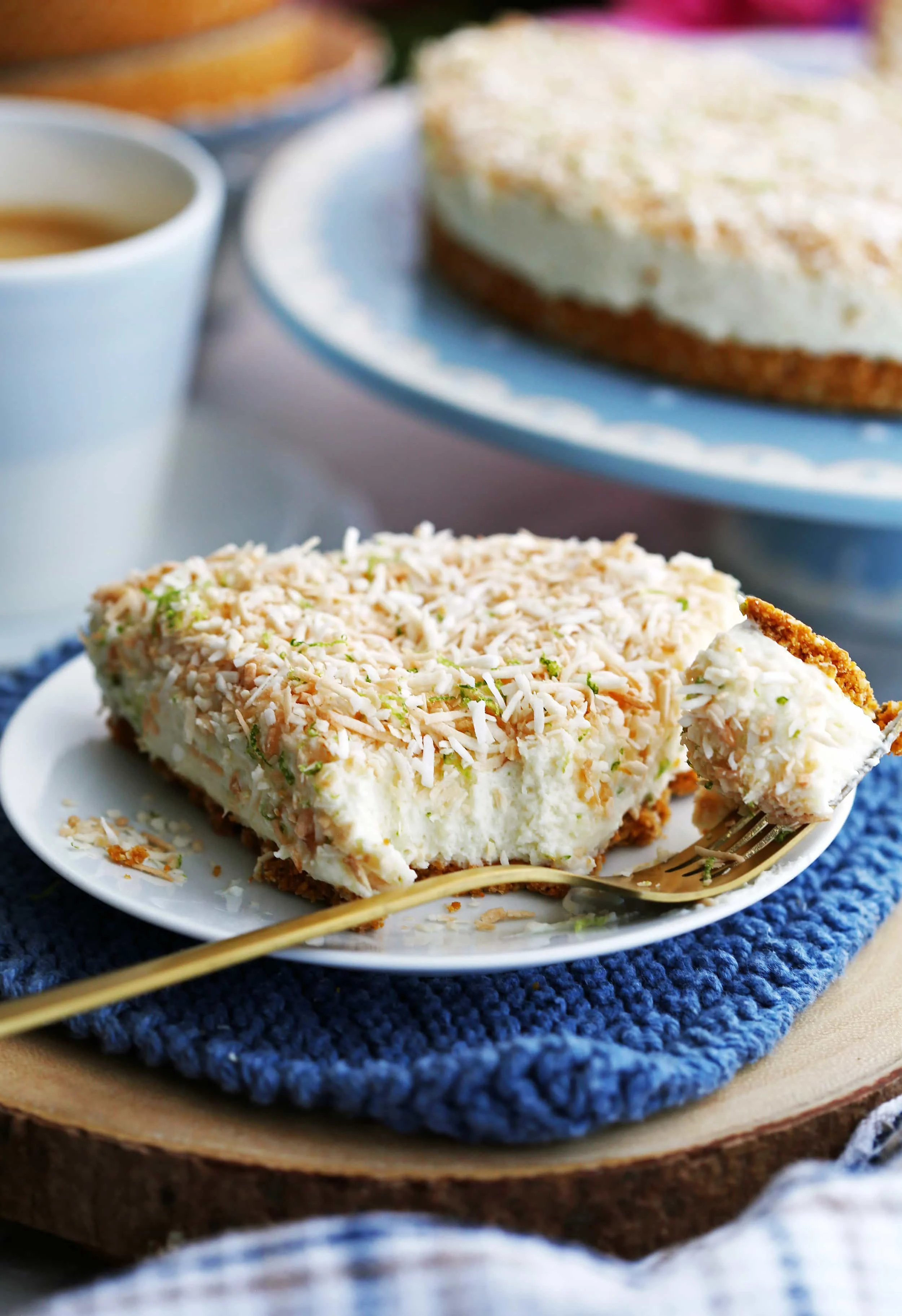 A closeup view of a slice of no-bake coconut lime mascarpone cheesecake on a white plate with a gold fork.