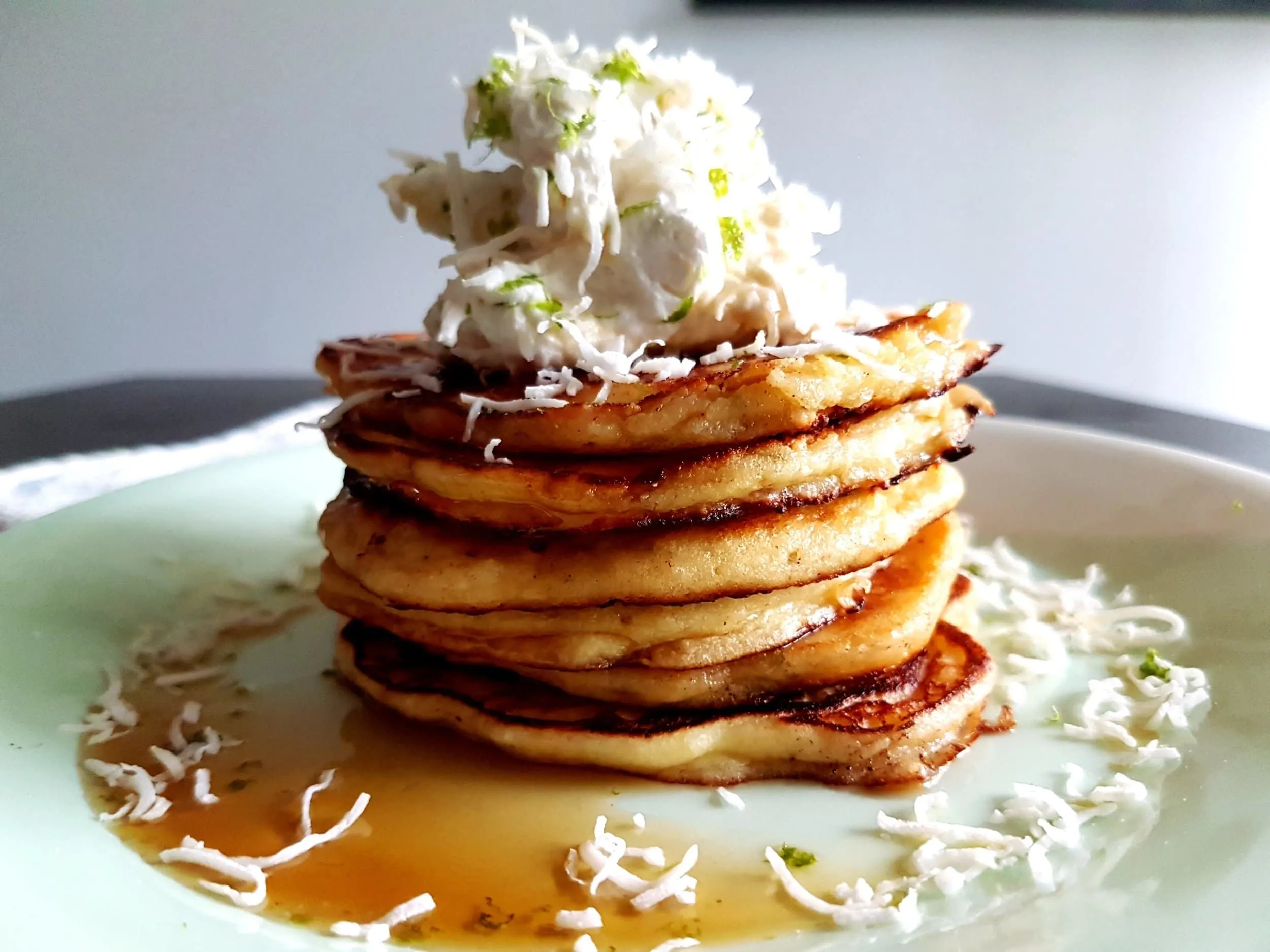 A stack of ricotta pancakes topped with coconut and lime whipped cream.