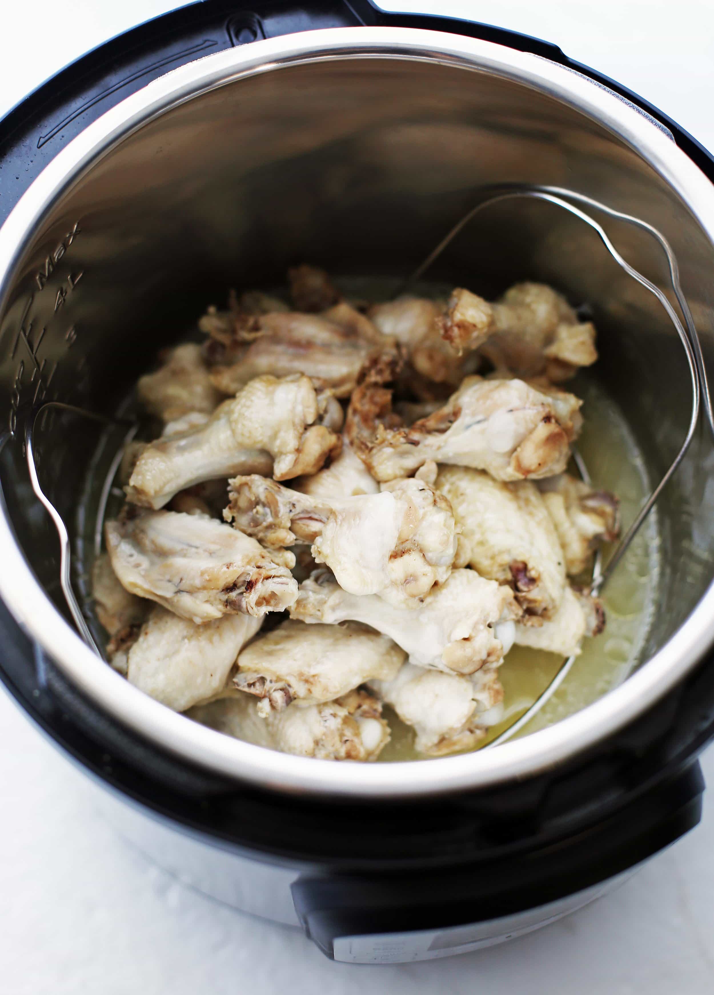 Cooked chicken wings piled on top of a metal trivet in the Instant Pot; a water and orange juice mixture under the trivet.