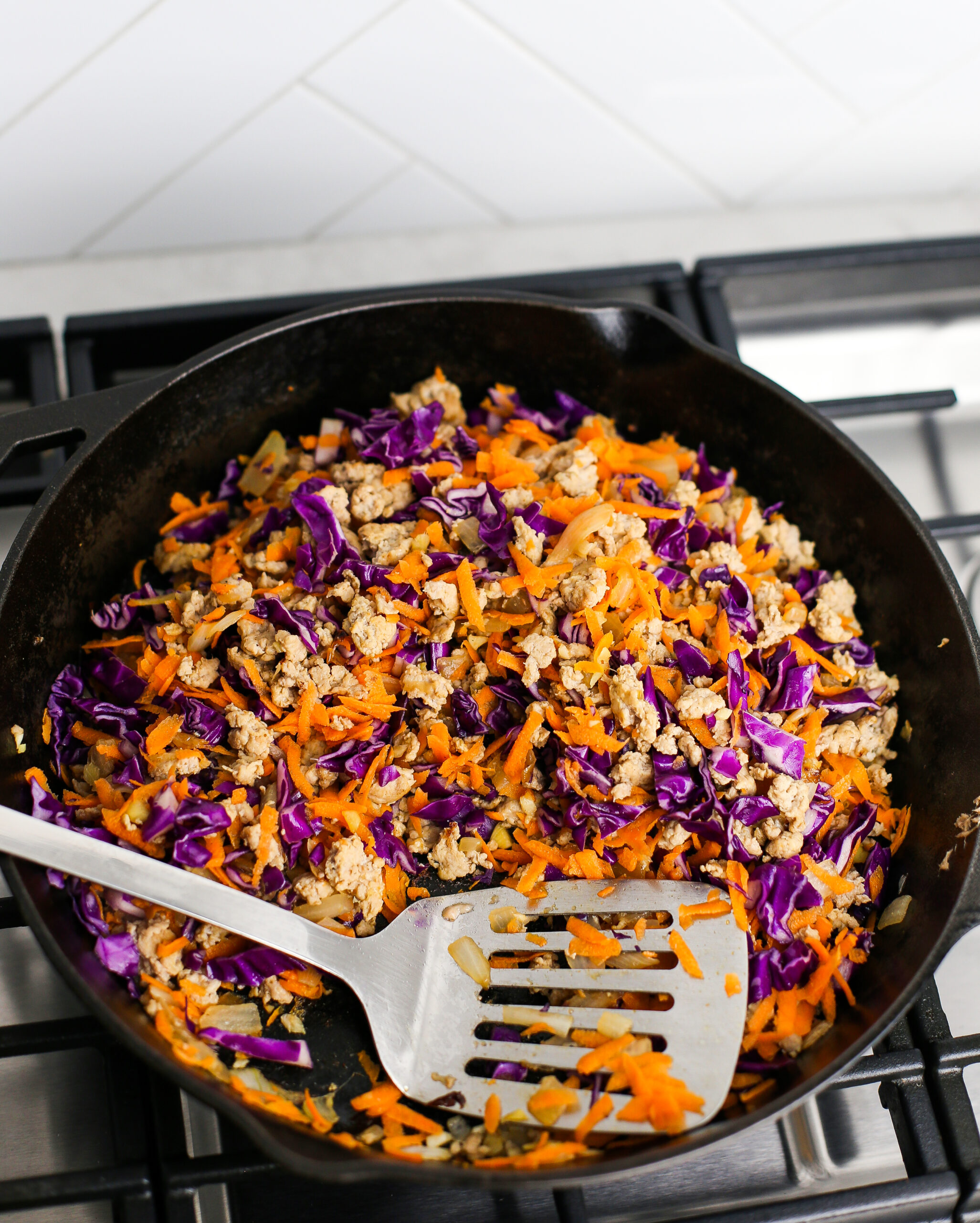 Ground chicken, chopped onions, shredded carrots and cabbage in a cast iron skillet.