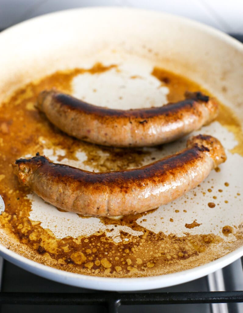 Two browned and cooked hot Italian sausages in a white frying pan.