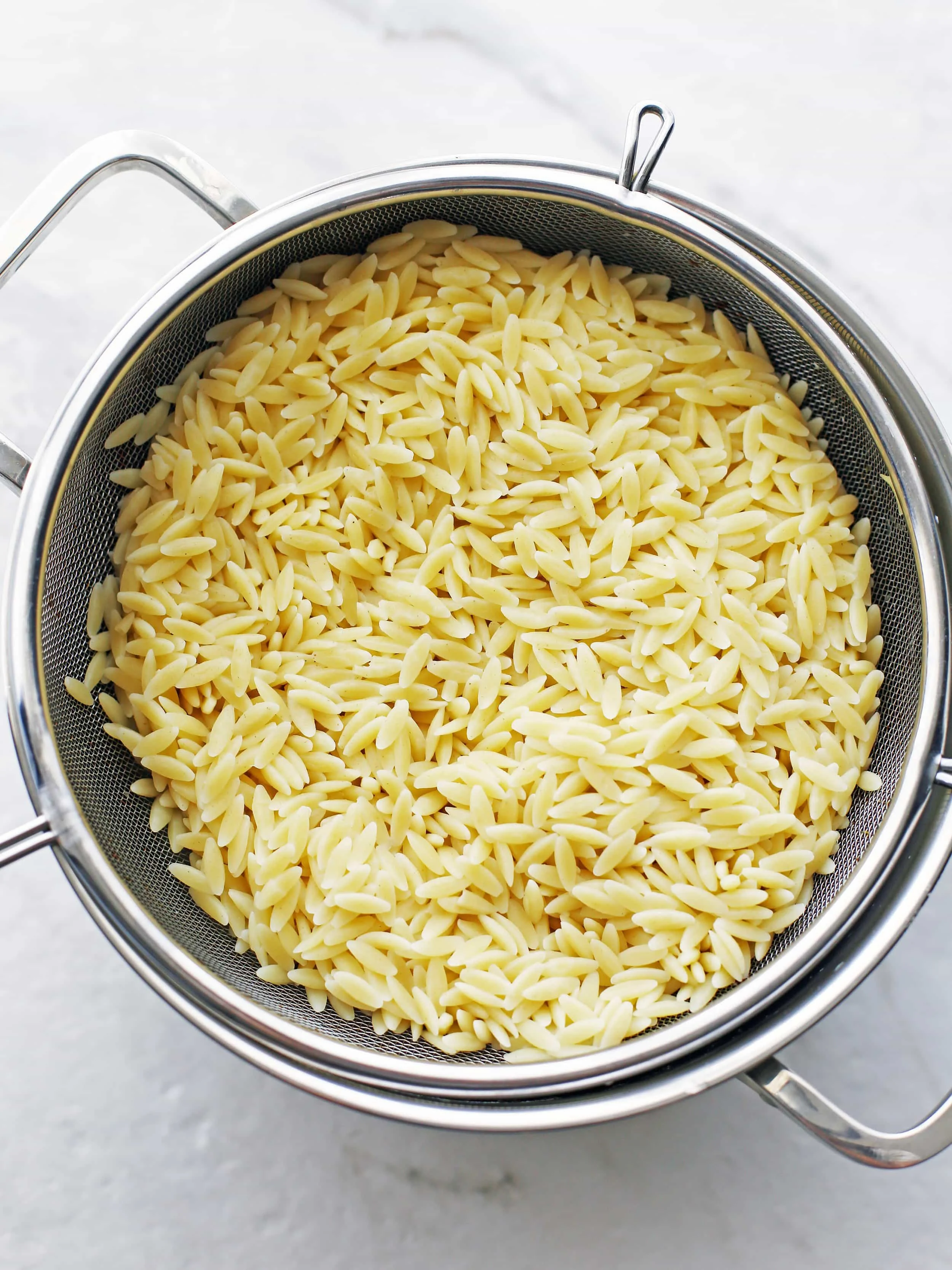 Cooked orzo pasta in a metal strainer that's been placed in a pot.