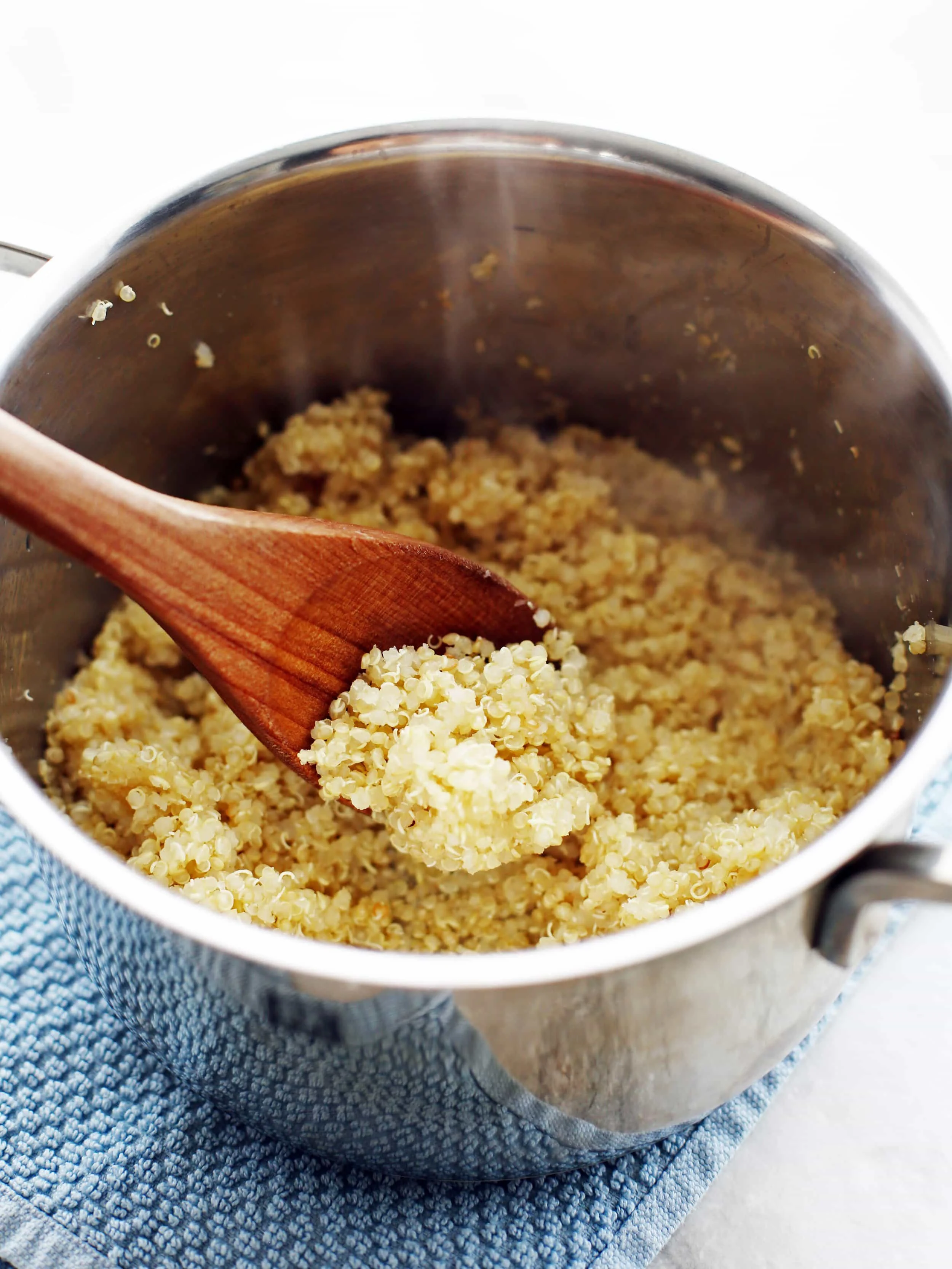 Cooked white quinoa in a small pot with a wooden spoon.