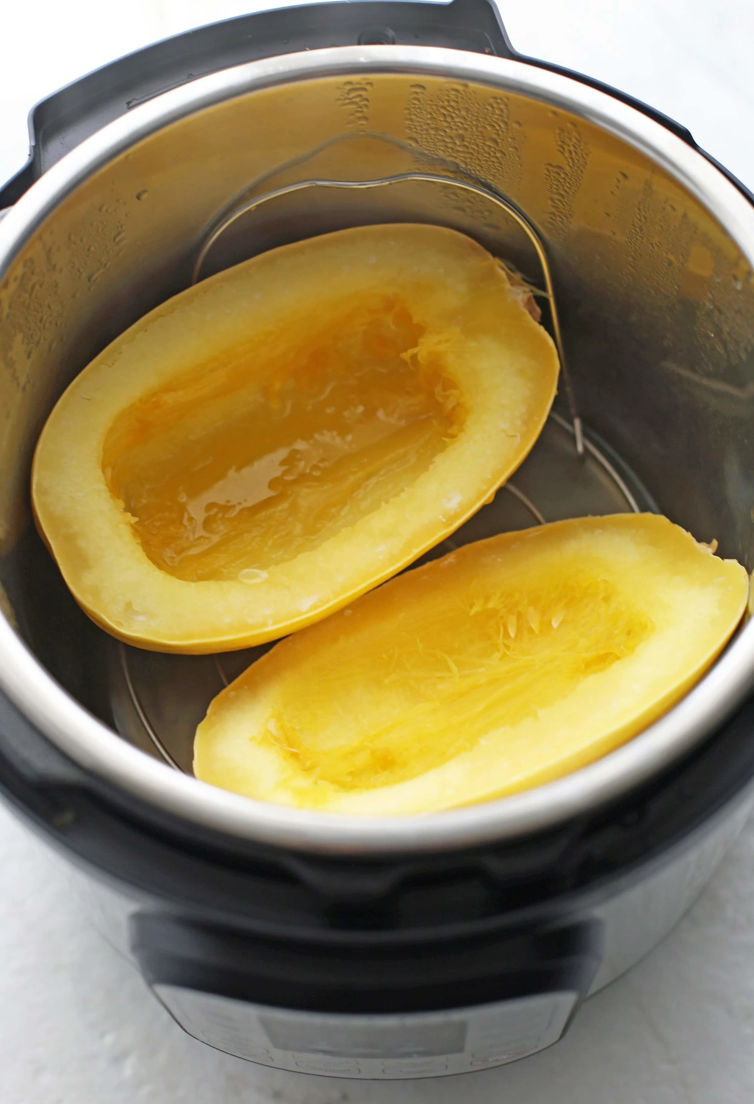 Cooked halved and seeded spaghetti squash cut side up on a metal trivet in the Instant Pot.