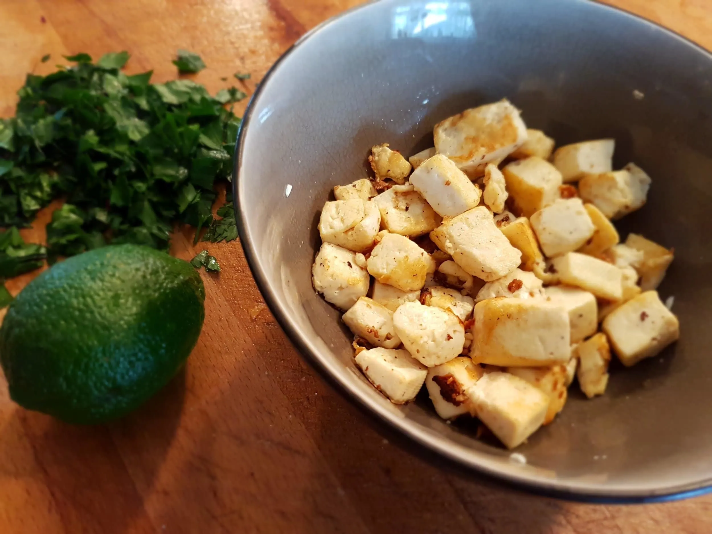 Cooked tofu in a bowl with parsley and lime on the side.
