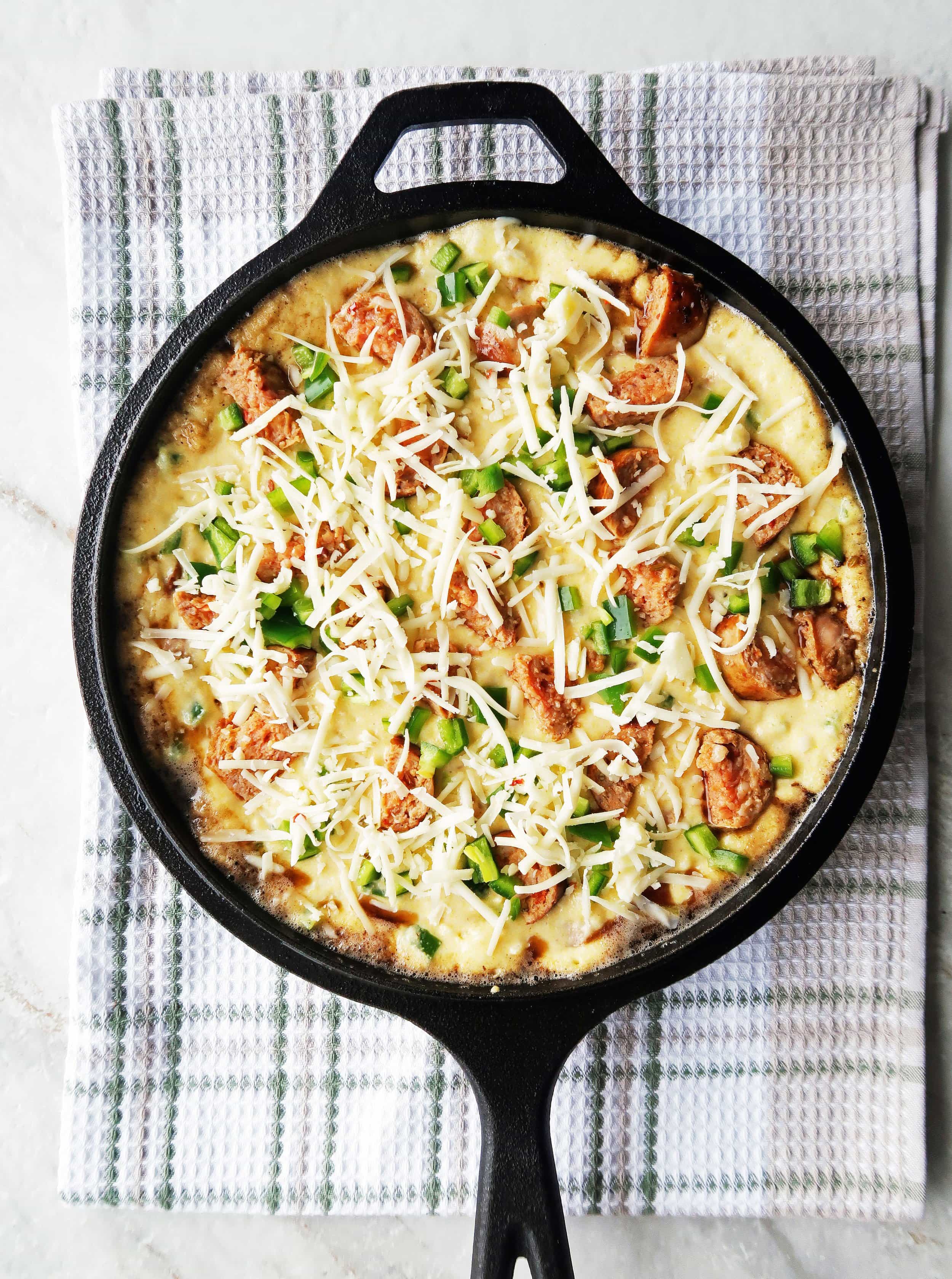 Jalapeño maple and sausage cornbread batter spread on a cast-iron skillet topped with cheese.