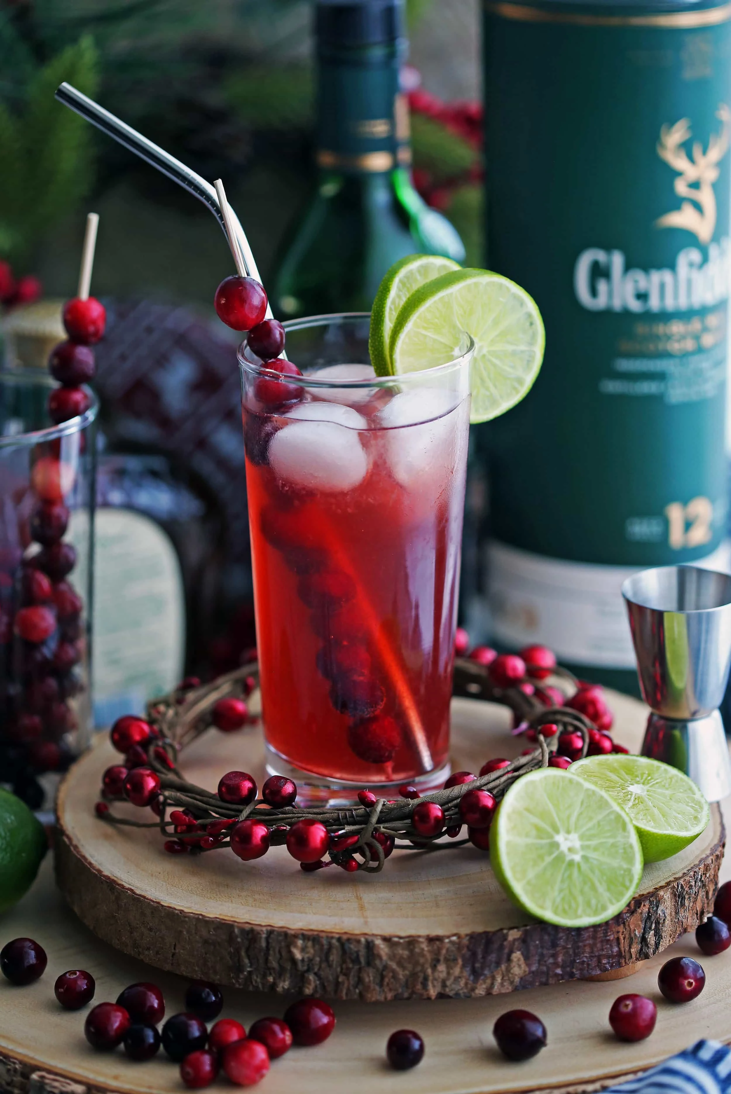 A tall highball glass full of Cranberry Whiskey Ginger Cocktail with lime slices and fresh cranberries.