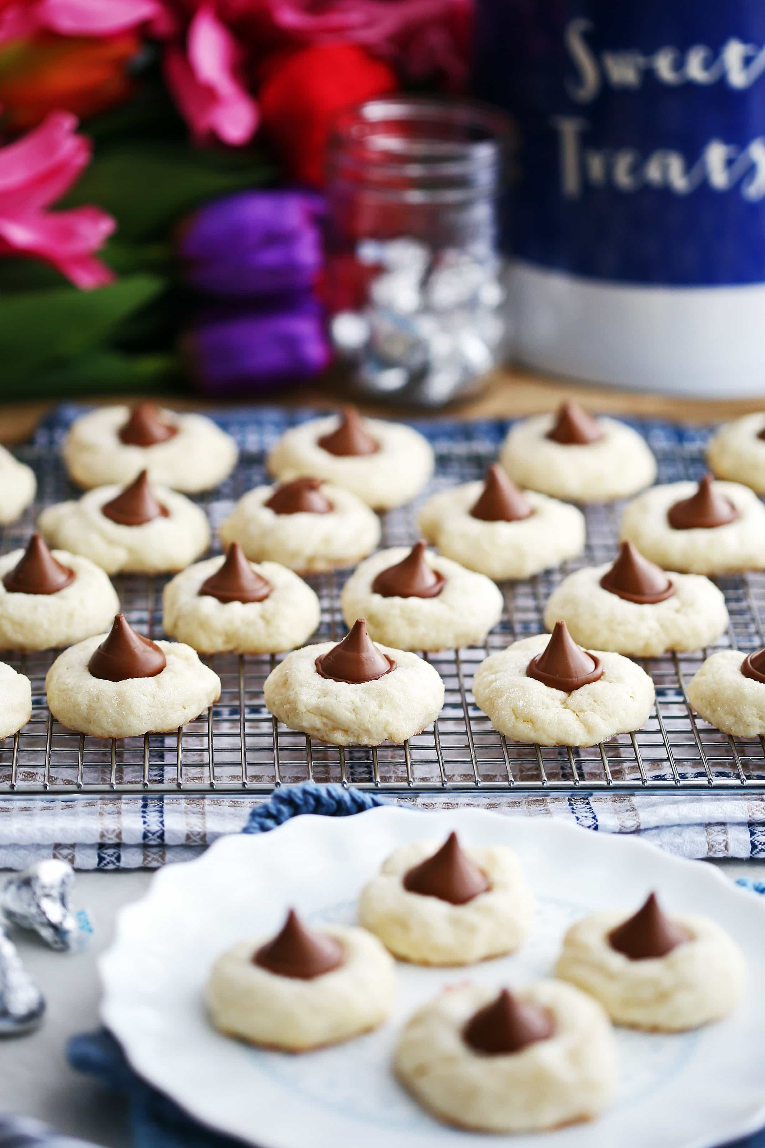 Cream cheese cookies with Hershey’s Kisses pressed on top on a cooling rack and white plate.