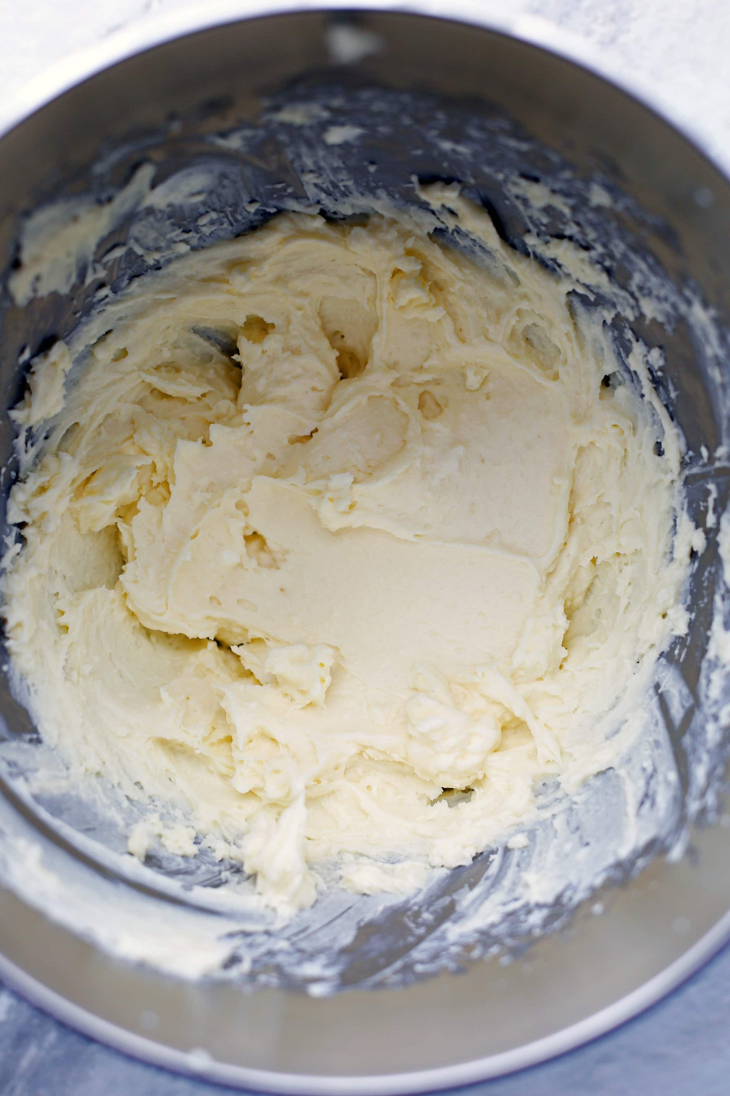 Butter, cream cheese, sugar, vanilla extract, and an egg combined in a large metal mixing bowl.