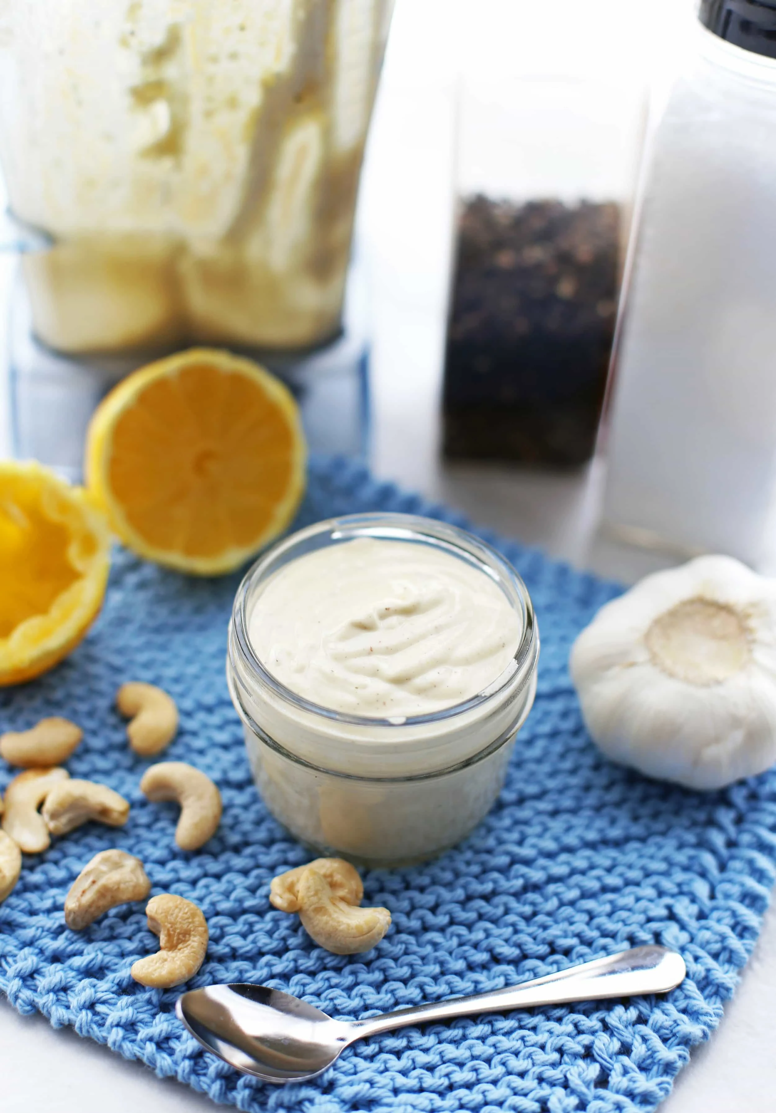 Creamy Garlic Cashew Dressing in a small mason jar that's surrounded by cashews, garlic, lemon, and a spoon.