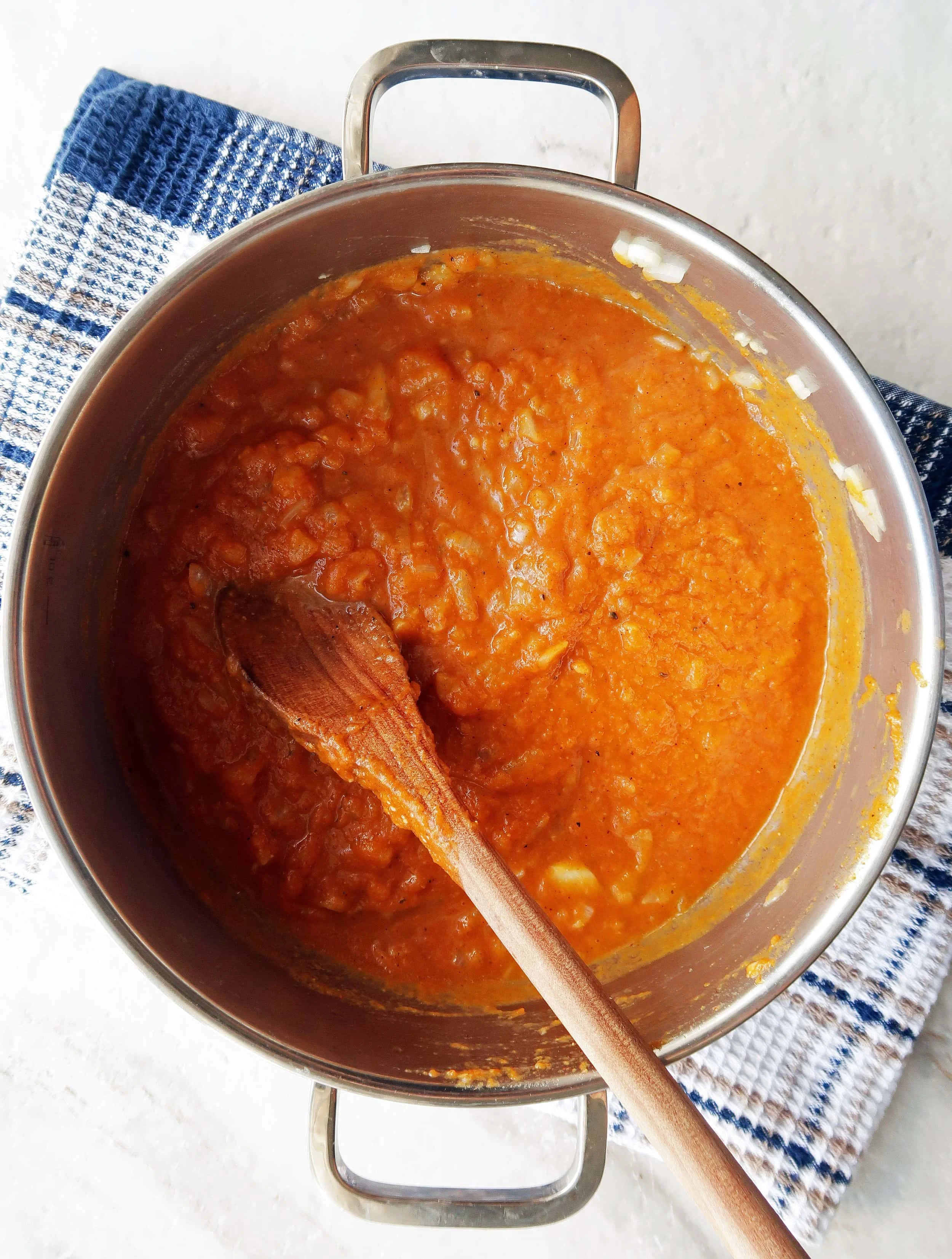 Sautéed onions and garlic with spiced pumpkin sauce in a large metal pot.